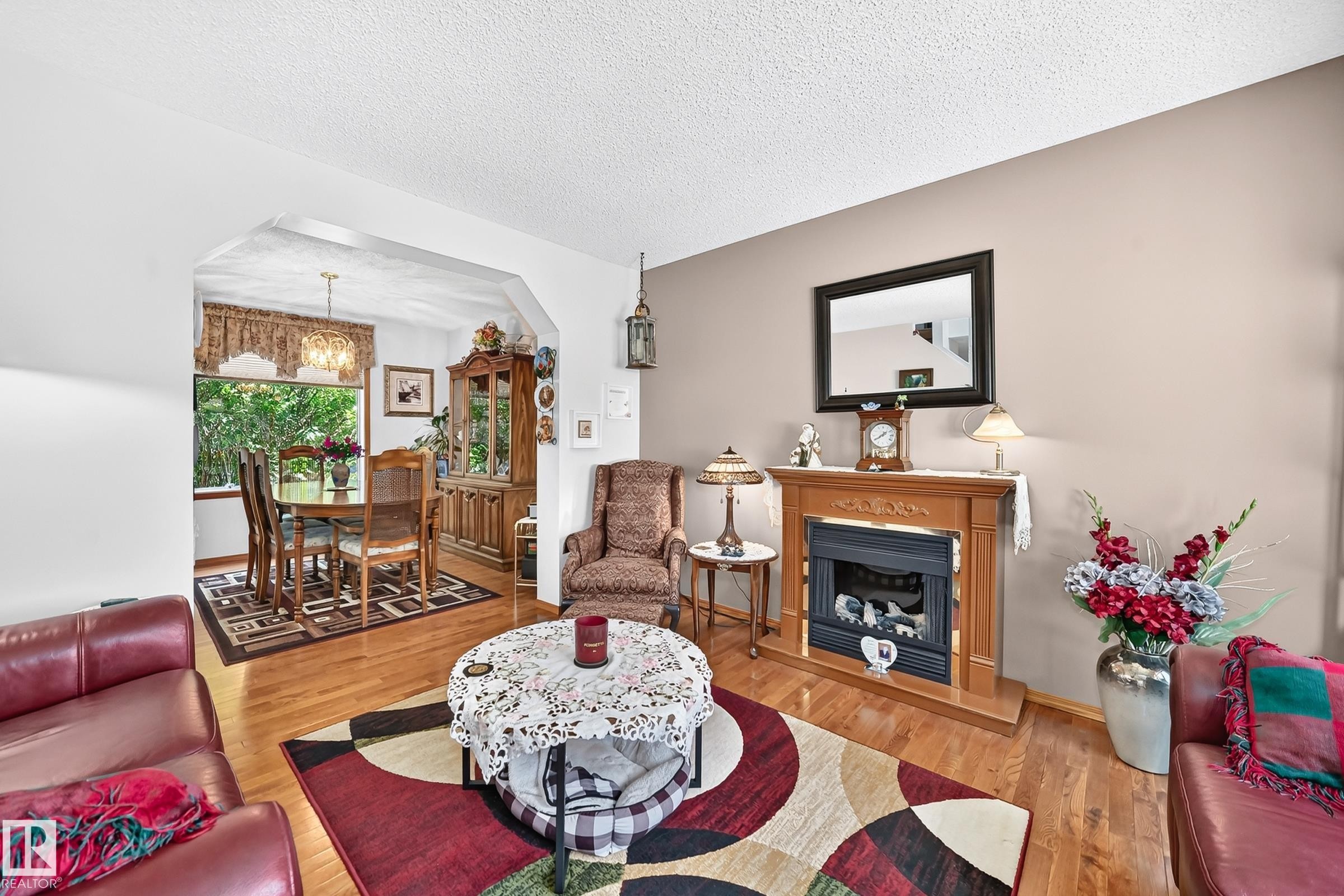Hardwood flooring throughout, a decorative fireplace, and an arched entry to the dining area - 13069 37 Street Nw, Edmonton, AB - Indoor Photo Showing Living Room With Fireplace
