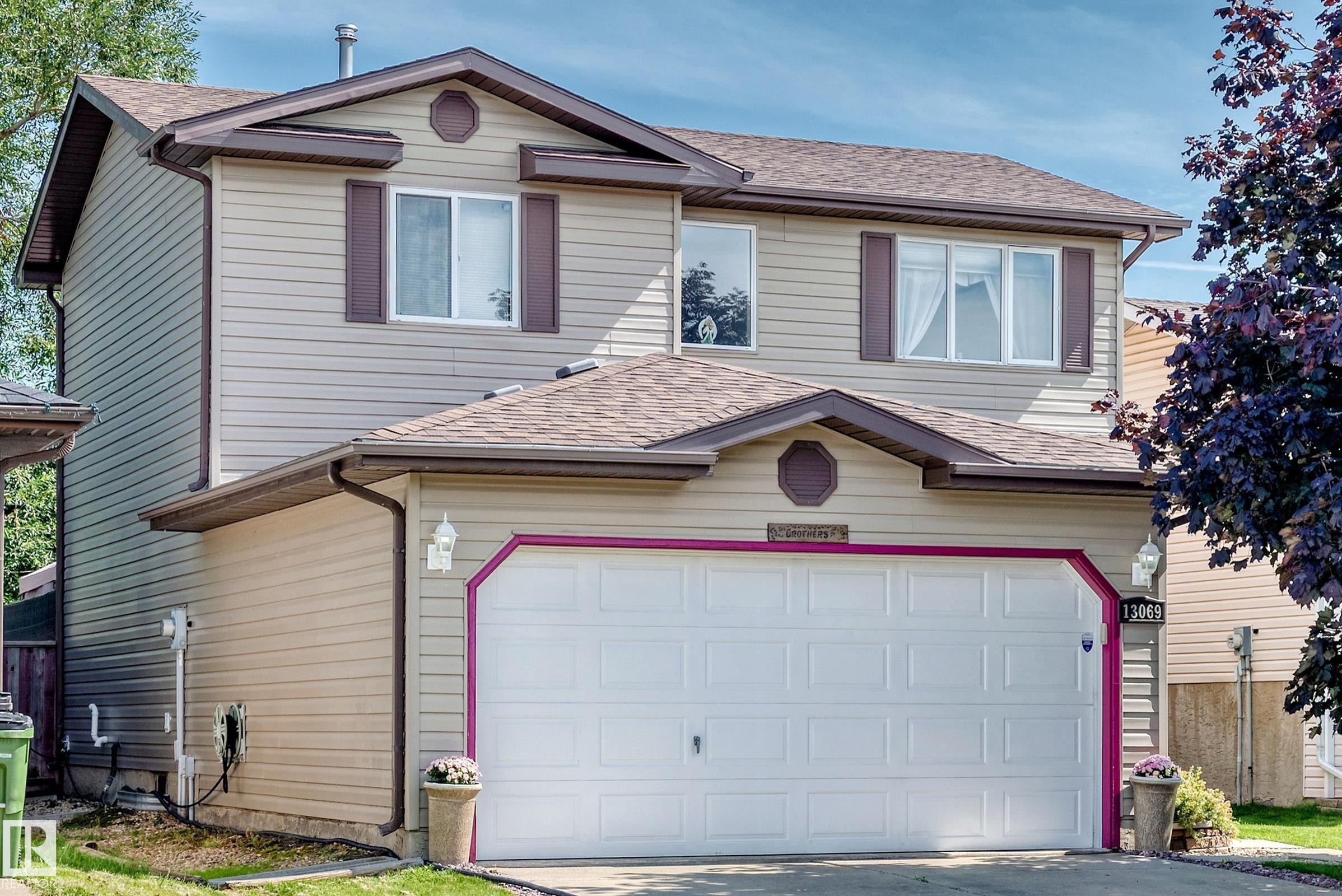 Two-story residence featuring light-toned horizontal siding, dark brown roofing, and a prominent double garage with a white door - 13069 37 Street Nw, Edmonton, AB - Outdoor With Exterior