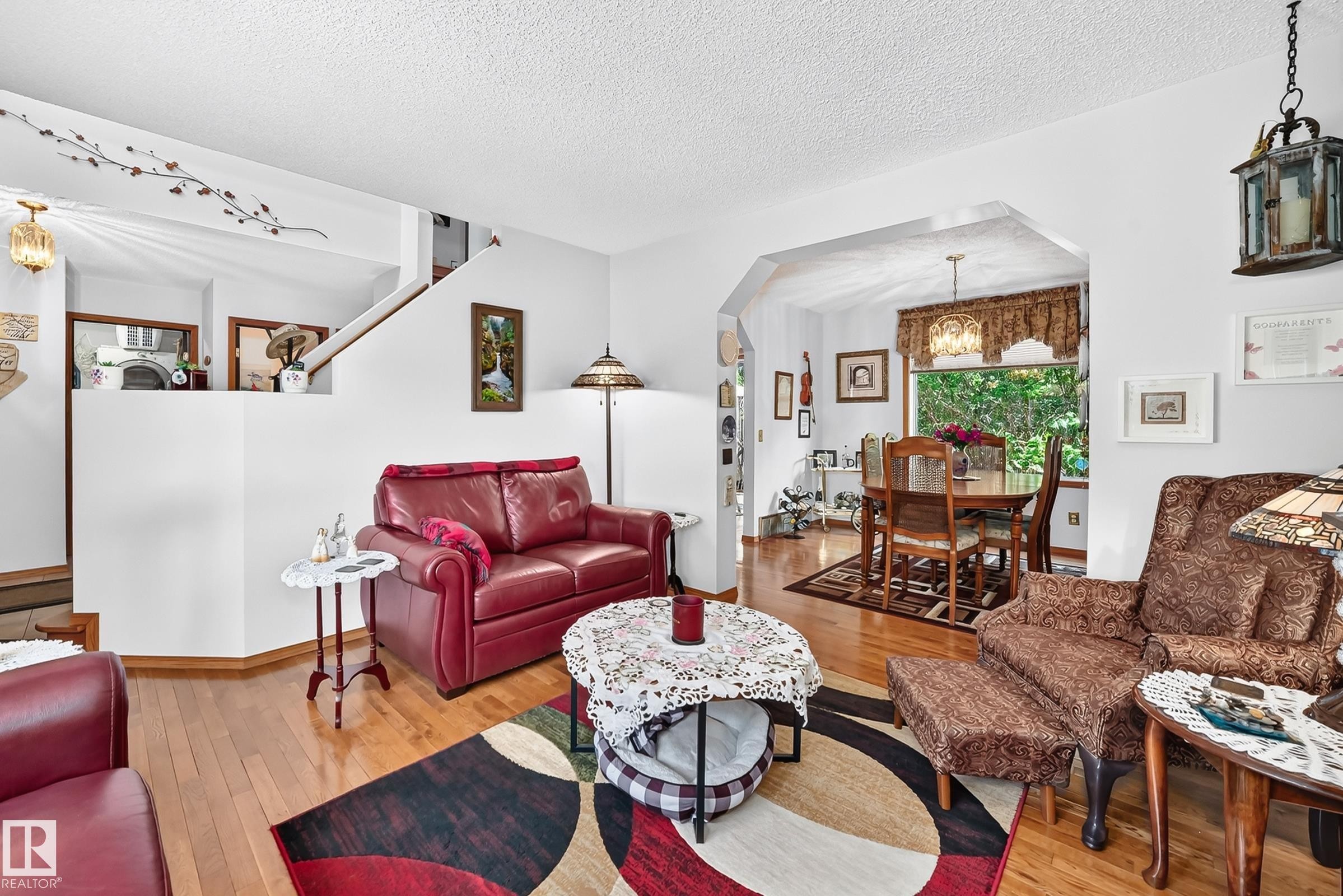 Hardwood flooring extends throughout the living area, featuring a half-wall partition and an arched entryway to the dining space - 13069 37 Street Nw, Edmonton, AB - Indoor Photo Showing Living Room