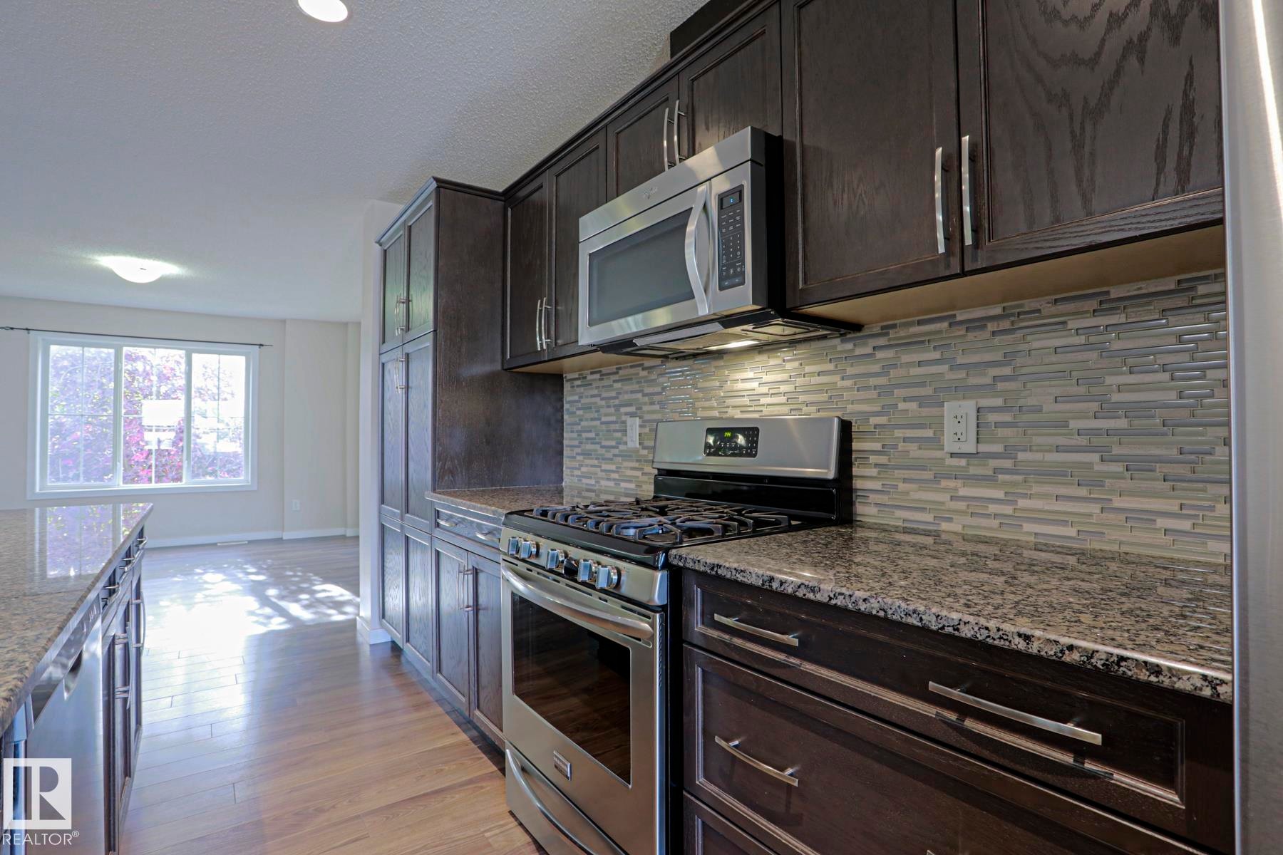 Kitchen featuring dark wood-finish cabinetry, stainless steel appliances, granite countertops, and a glass tile backsplash - 308 Watt Boulevard Sw, Edmonton, AB - Indoor Photo Showing Kitchen With Upgraded Kitchen
