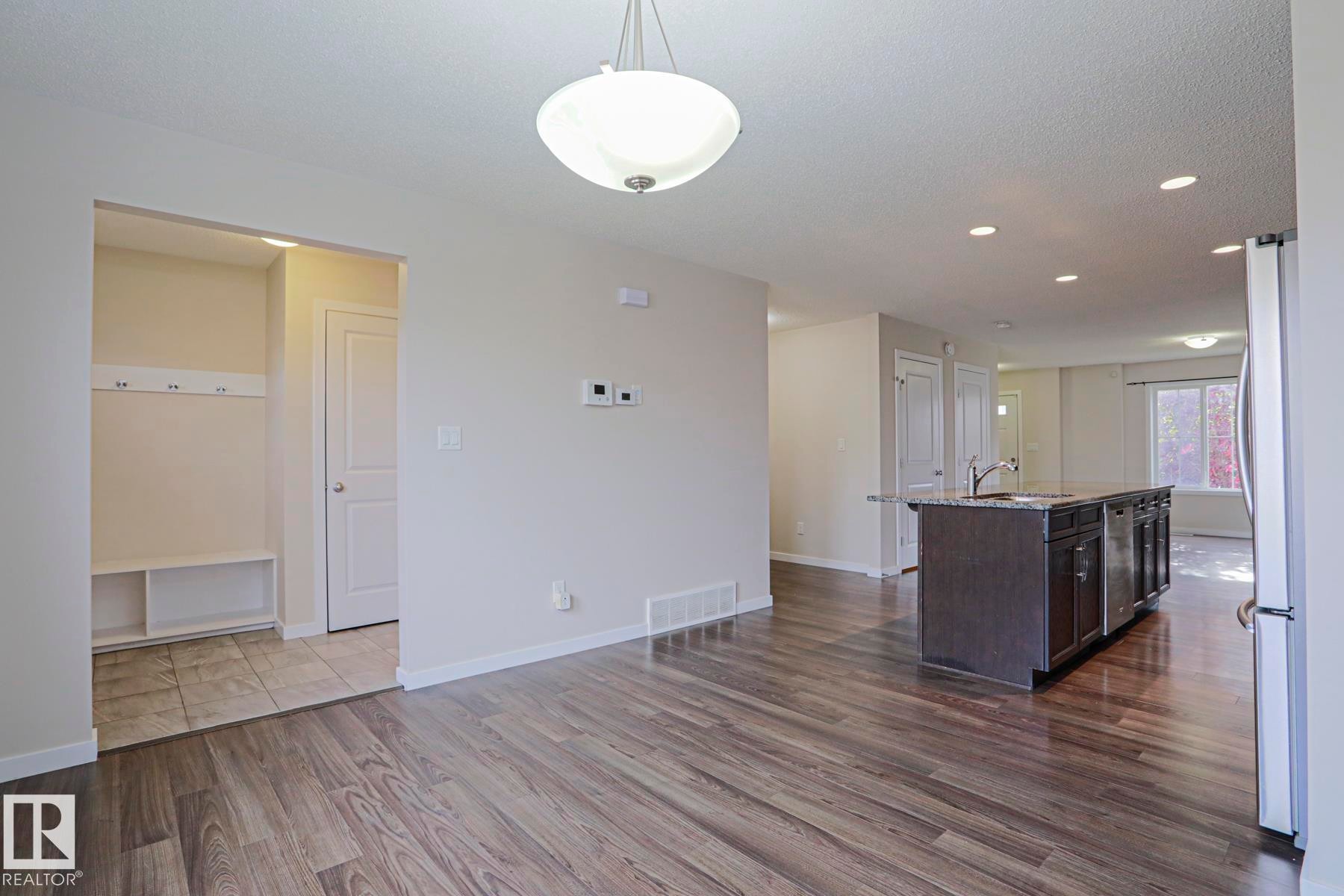 Open-concept living area featuring wood-finish flooring, recessed lighting, a modern pendant light, and a kitchen island with built-in cabinetry and an integrated sink - 308 Watt Boulevard Sw, Edmonton, AB - Indoor