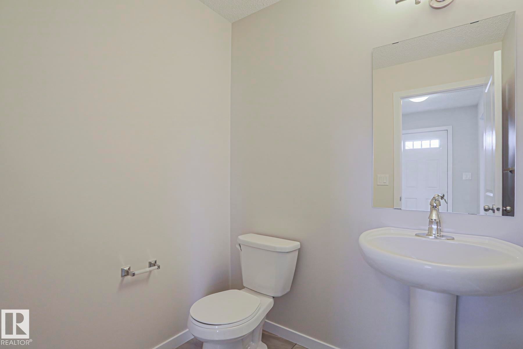 Clean and bright half bathroom featuring a pedestal sink with chrome faucet, a two-piece toilet with closed lid, and neutral wall finishes - 308 Watt Boulevard Sw, Edmonton, AB - Indoor Photo Showing Bathroom