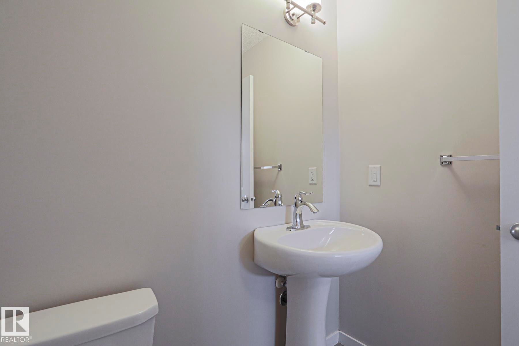 Pedestal sink with chrome faucet, rectangular mirror, and wall-mounted light fixture - 308 Watt Boulevard Sw, Edmonton, AB - Indoor Photo Showing Bathroom