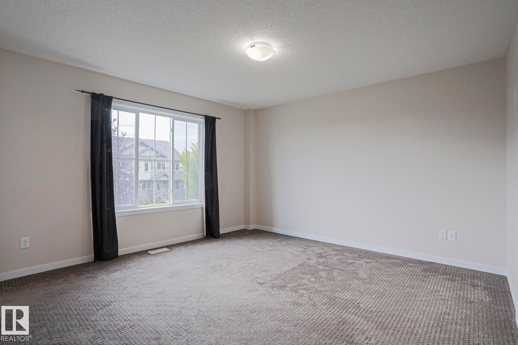 Neutral wall paint, textured carpeting, large window with white trim, and a ceiling-mounted light fixture - 308 Watt Boulevard Sw, Edmonton, AB - Indoor Photo Showing Other Room