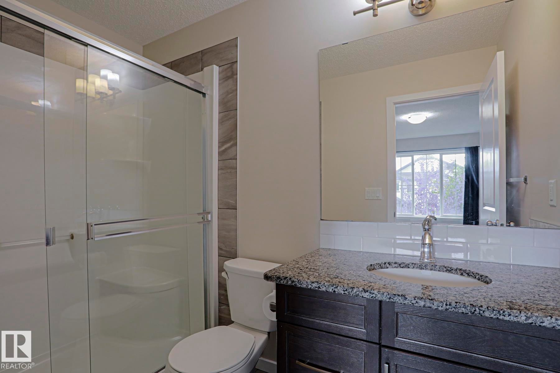 Shower with glass enclosure, single vanity with granite countertop, white subway tile backsplash, and a wall-mounted mirror - 308 Watt Boulevard Sw, Edmonton, AB - Indoor Photo Showing Bathroom