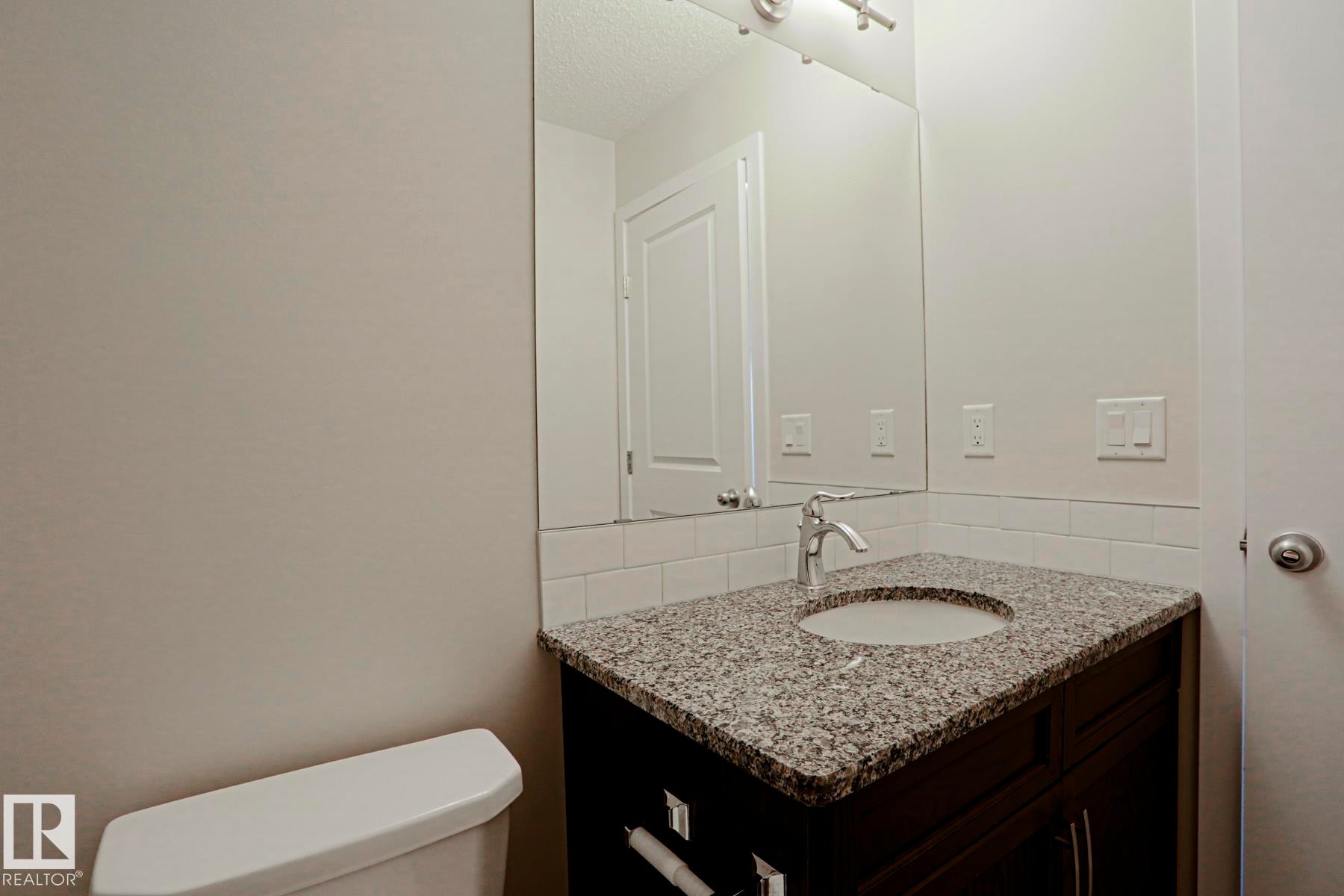 Vanity with a polished chrome faucet, under-mount sink, and speckled countertop, white subway tile backsplash, and a wall-mounted mirror - 308 Watt Boulevard Sw, Edmonton, AB - Indoor Photo Showing Bathroom