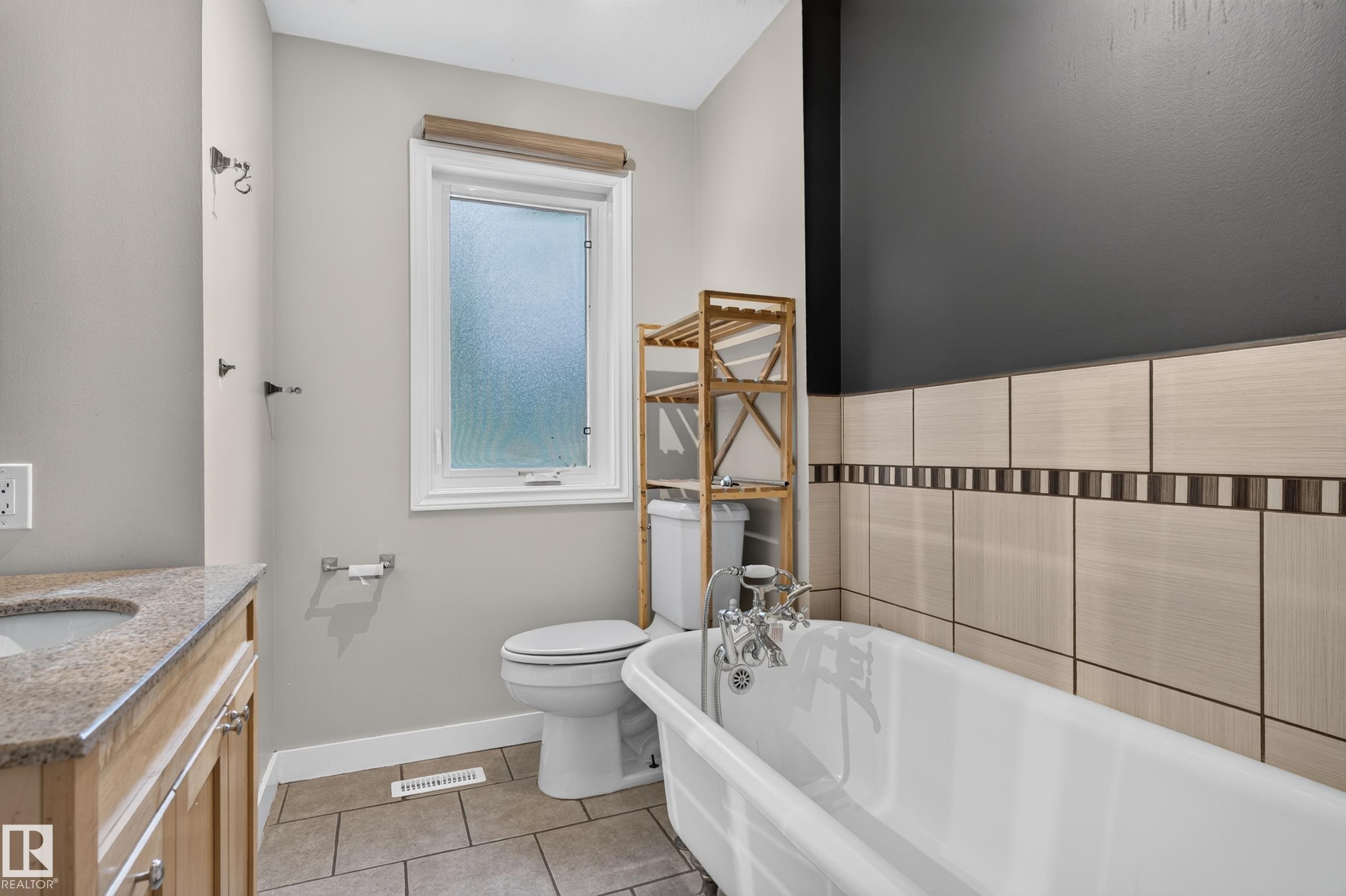 Freestanding bathtub with chrome fixtures, tiled wall surround, and a vanity with a stone countertop - 11549 88 Street Nw, Edmonton, AB - Indoor Photo Showing Bathroom