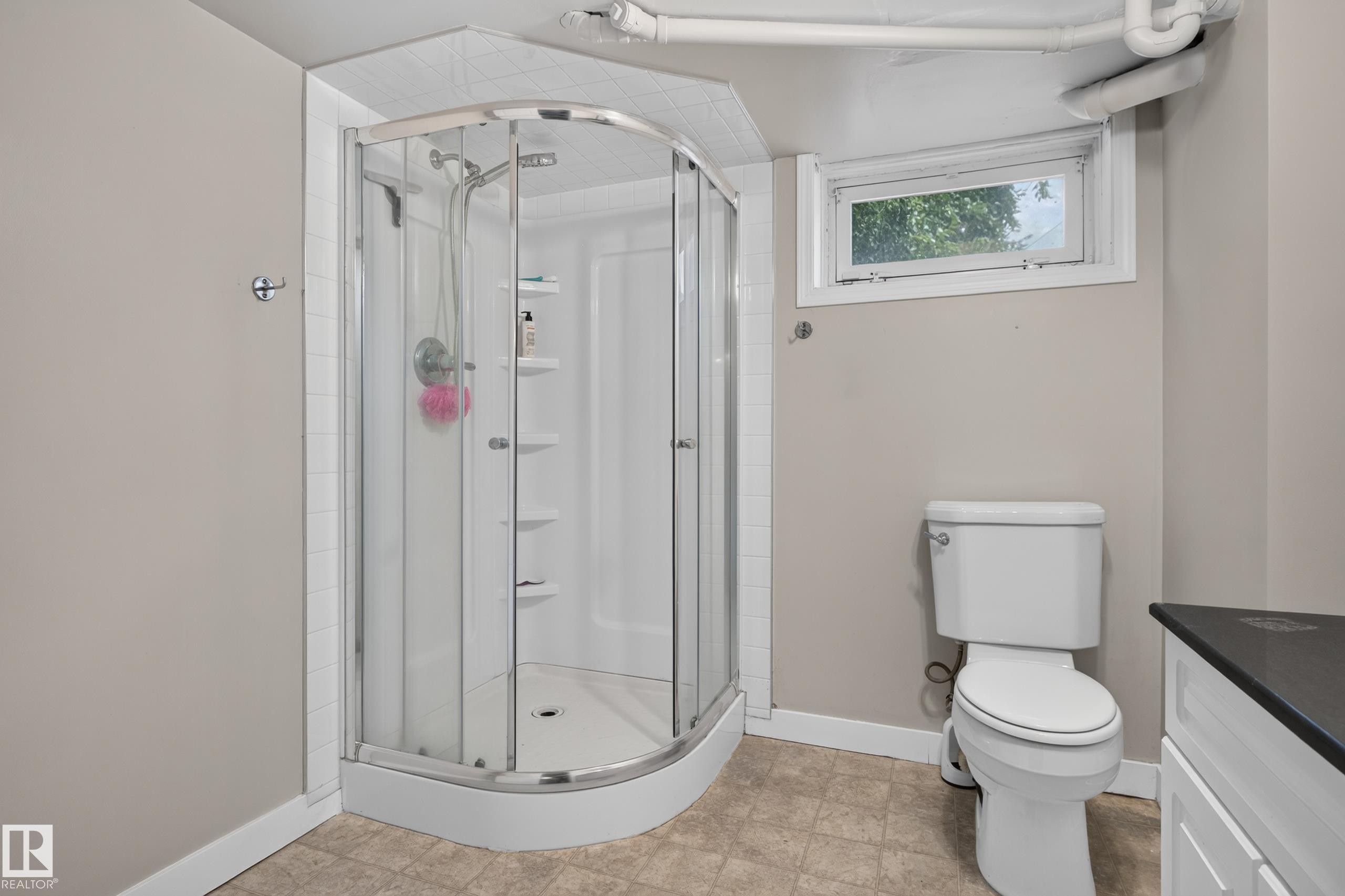 Compact corner shower enclosure with a curved glass door, white acrylic base, and integrated shelving - 11549 88 Street Nw, Edmonton, AB - Indoor Photo Showing Bathroom