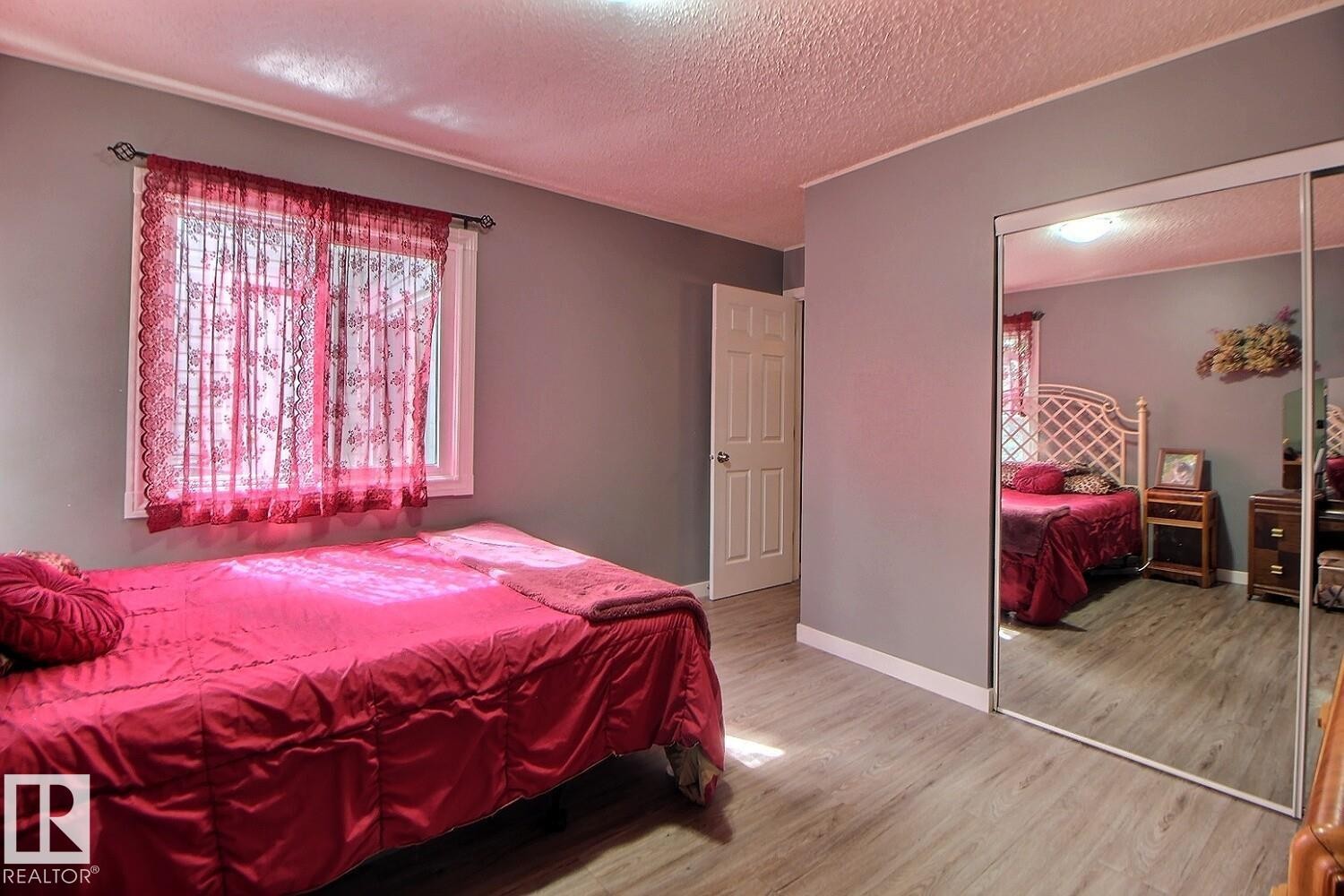 Window with white trim, wood-finish flooring, and mirrored closet doors - #304 14004 26 St Nw, Edmonton, AB - Indoor Photo Showing Bedroom