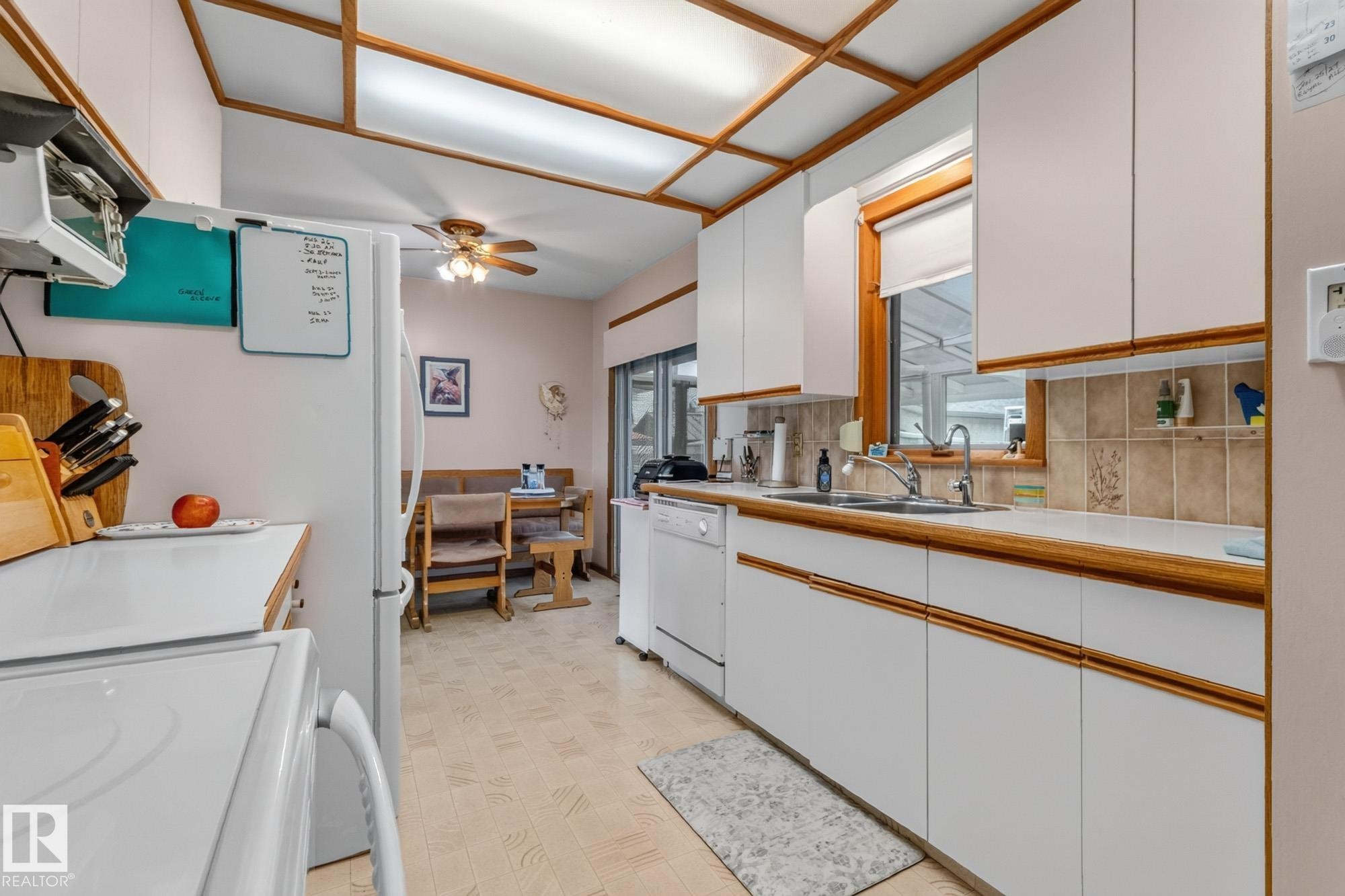 White cabinetry with wood-finish trim, ceramic tile backsplash, dual basin stainless steel sink, and a multi-pane window - 13432 134 Street Nw, Edmonton, AB - Indoor