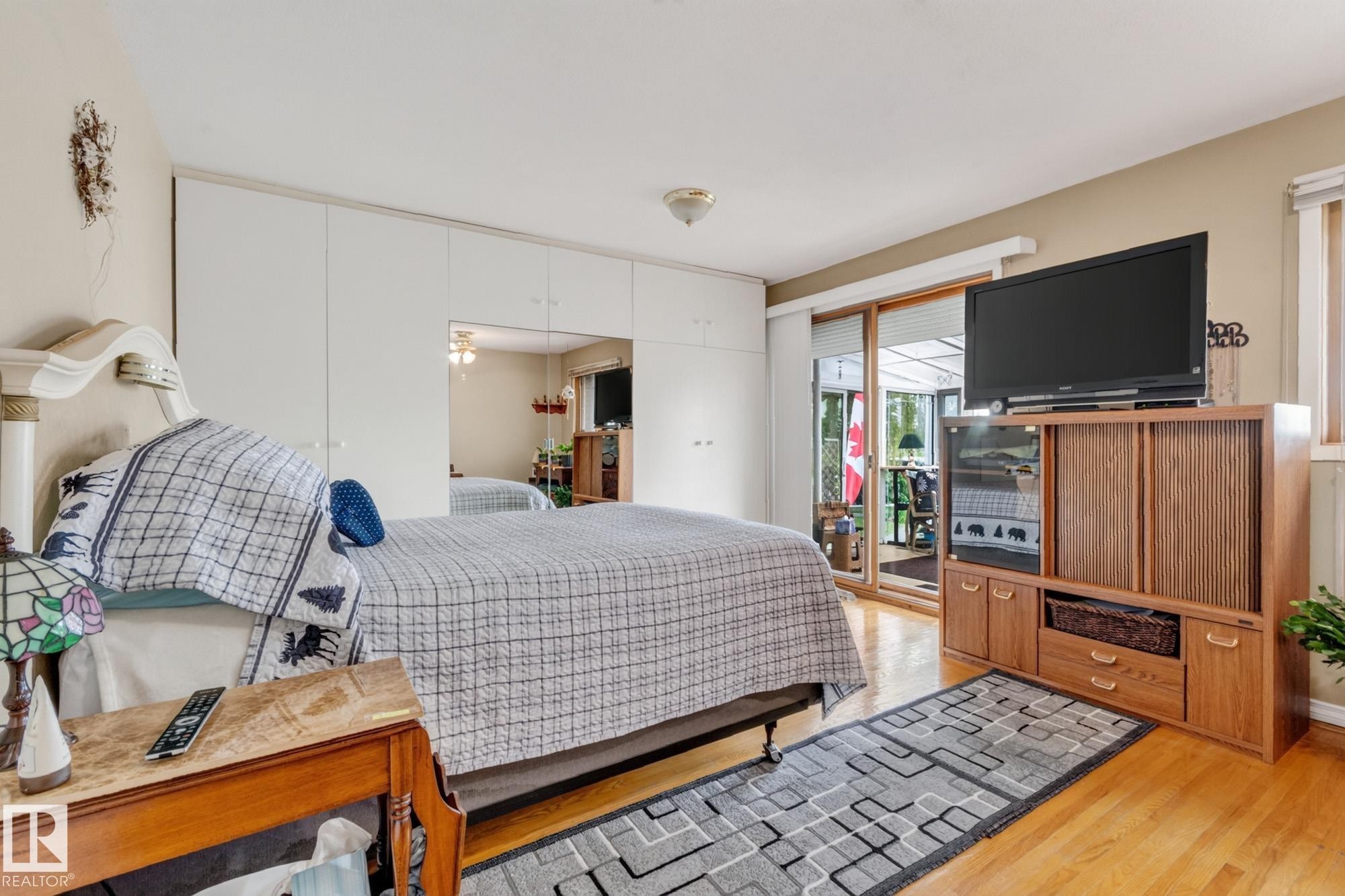 Light wood-finish flooring with built-in white cabinetry featuring mirrored panels and sliding glass doors - 13432 134 Street Nw, Edmonton, AB - Indoor Photo Showing Bedroom