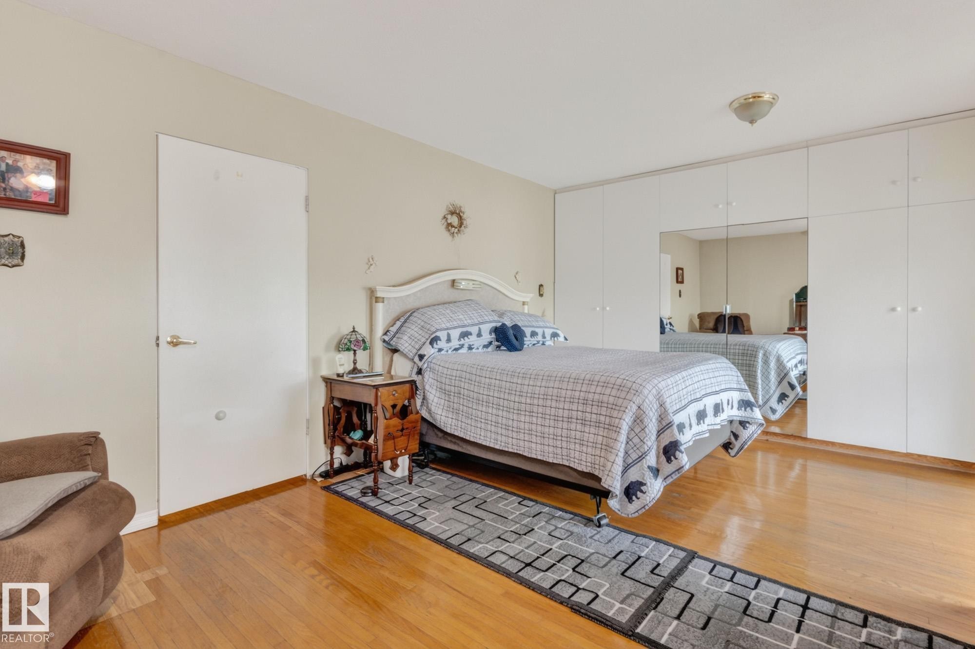 Built-in wall cabinetry with mirrored panels, wood-finish flooring, and semi-flush mount ceiling light - 13432 134 Street Nw, Edmonton, AB - Indoor Photo Showing Bedroom