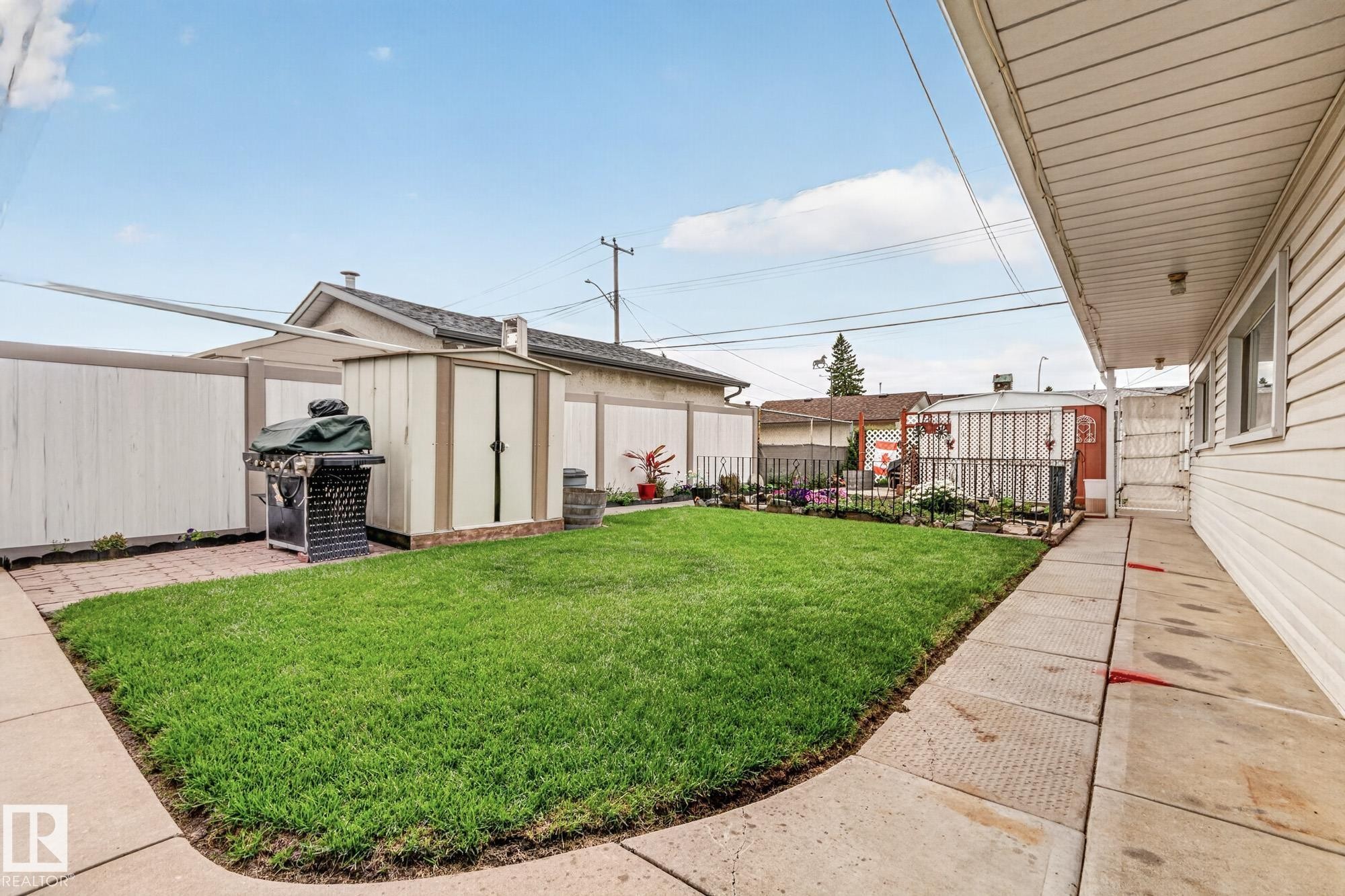 Grassed backyard area featuring a storage shed, concrete patio, and perimeter fencing - 13432 134 Street Nw, Edmonton, AB - Outdoor