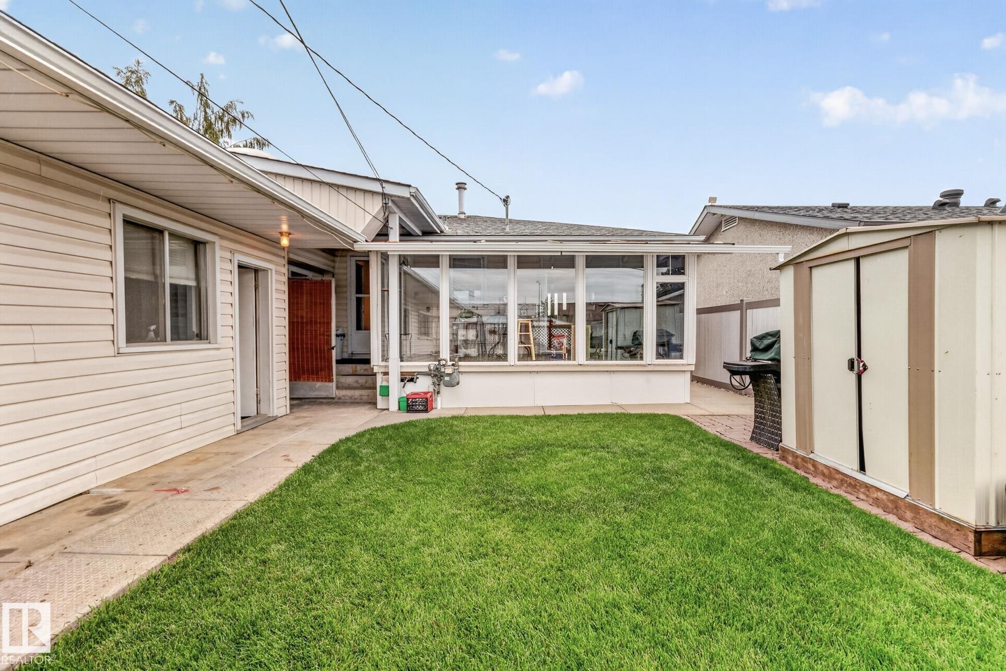 Expansive green lawn, enclosed patio structure with large windows, exterior storage shed, and a concrete pathway - 13432 134 Street Nw, Edmonton, AB - Outdoor With Deck Patio Veranda
