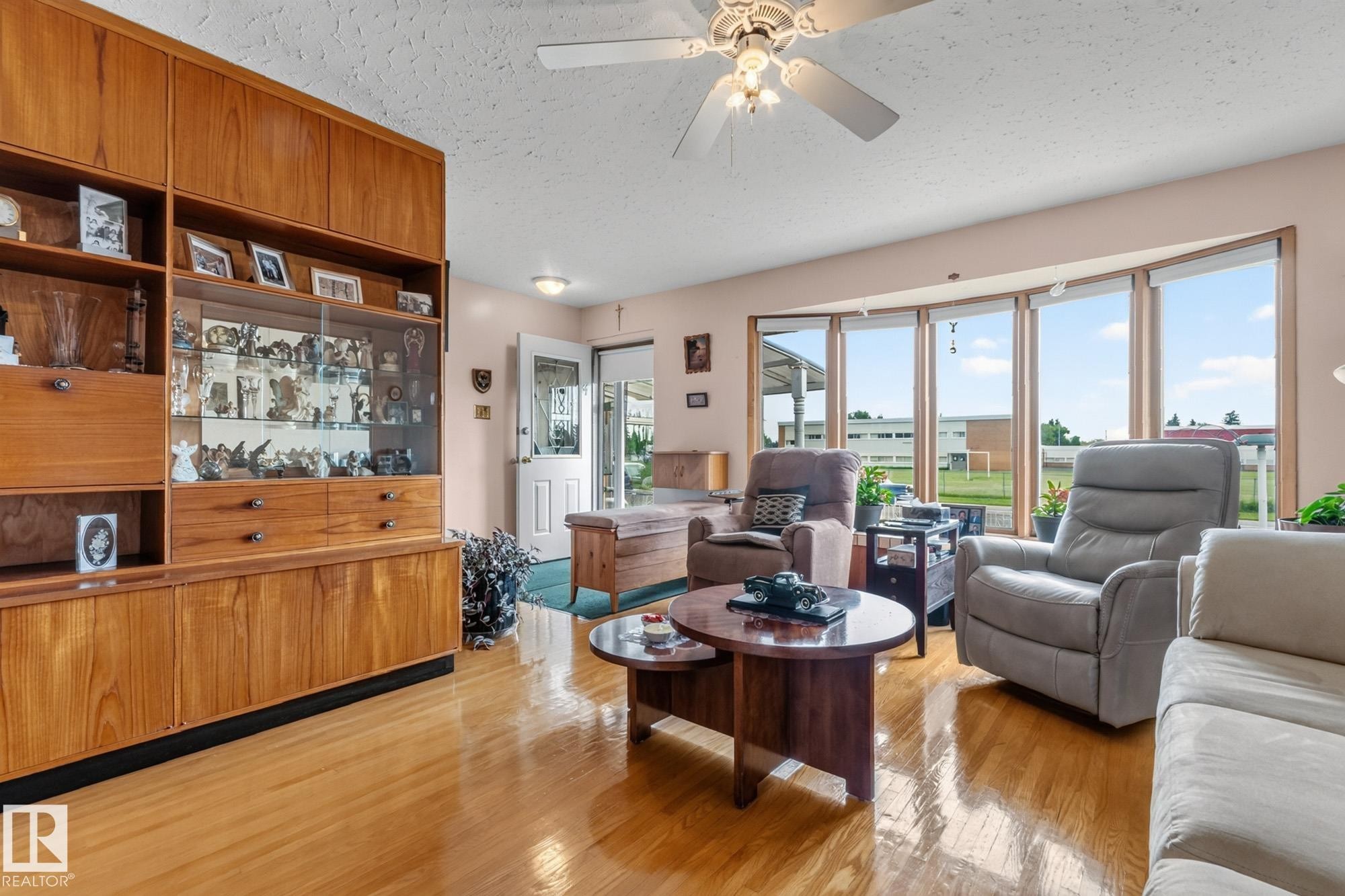 Expansive bay window, wood-finish flooring, built-in display cabinetry, ceiling fan, and paneled entry door - 13432 134 Street Nw, Edmonton, AB - Indoor Photo Showing Living Room