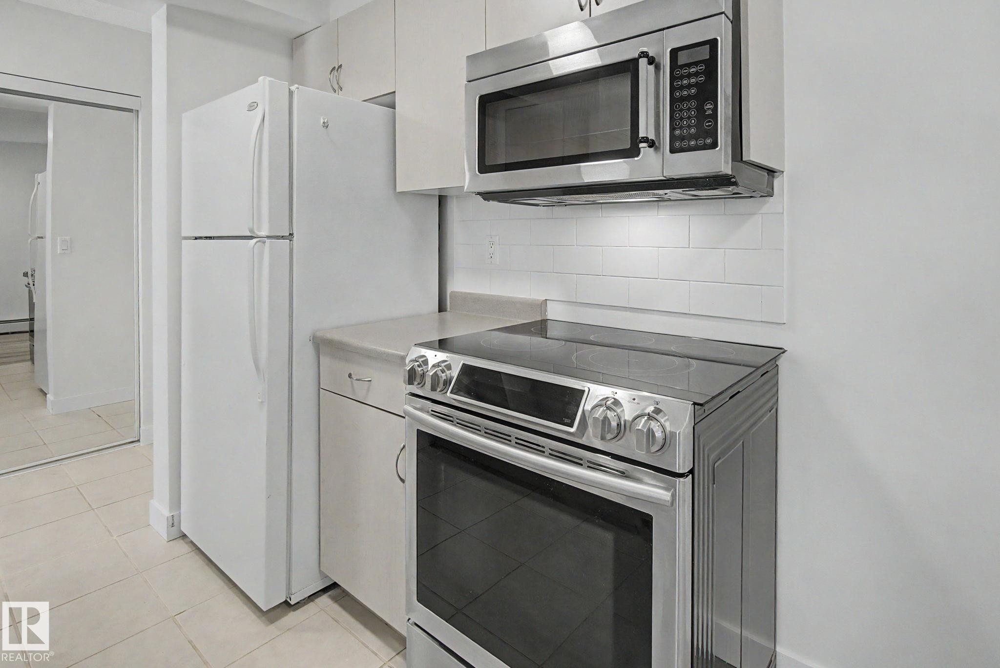 White cabinetry, stainless steel range, built-in microwave, subway tile backsplash, and light-toned countertops - #226 17011 67 Av Nw, Edmonton, AB - Indoor Photo Showing Kitchen