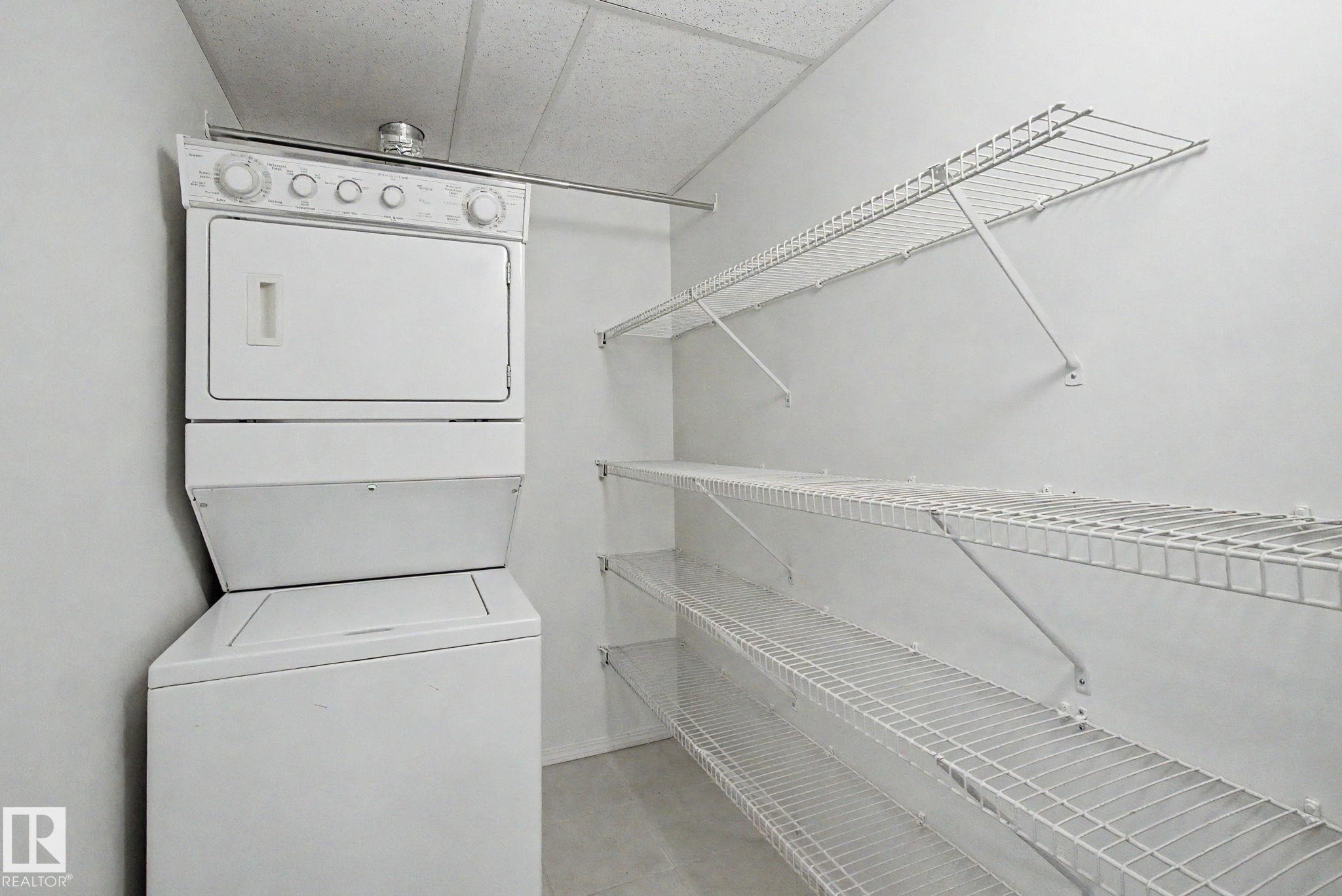 Laundry area featuring a stacked washer and dryer, wire shelving, and a hanging rod - #226 17011 67 Av Nw, Edmonton, AB - Indoor Photo Showing Laundry Room