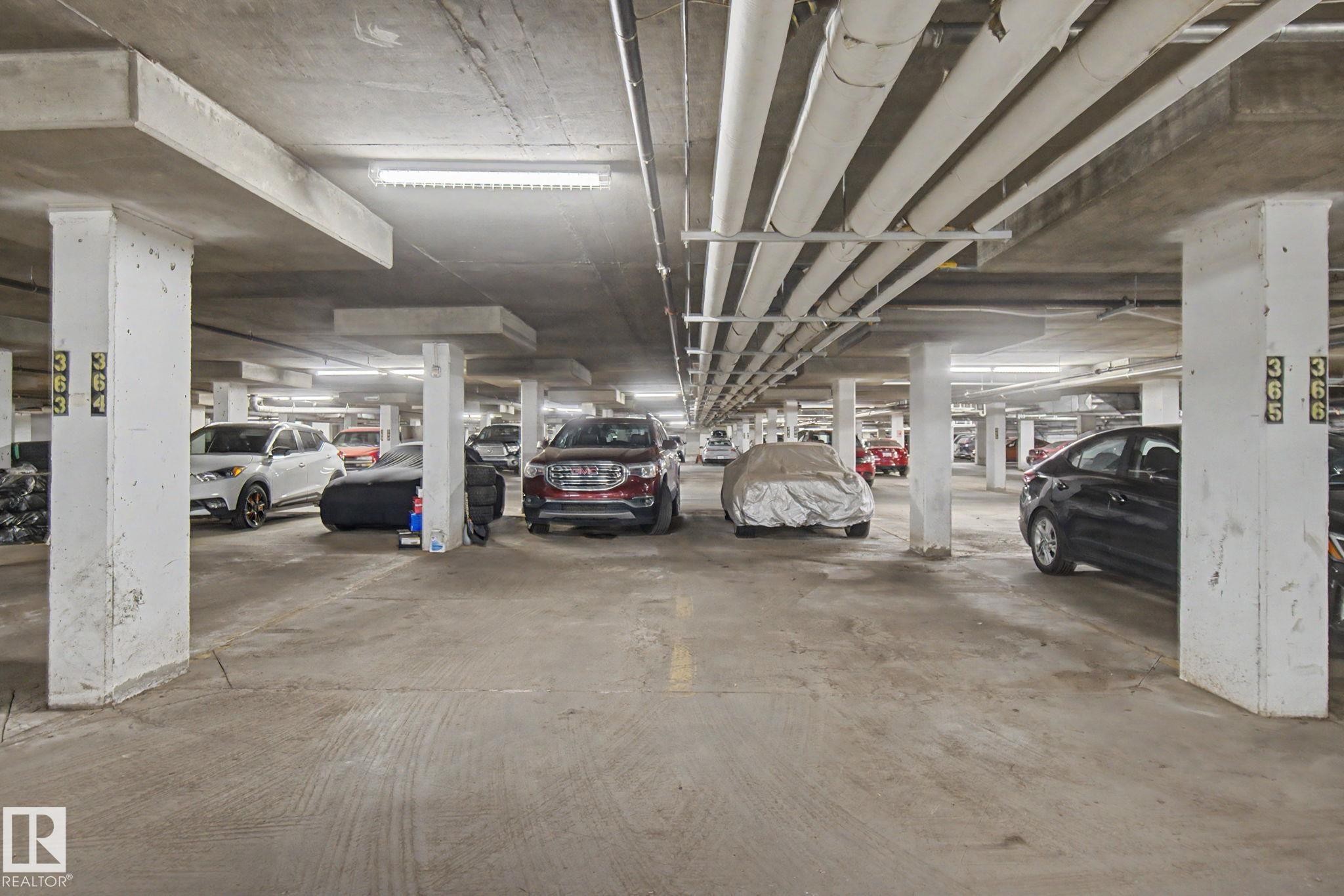 Concrete parking structure featuring overhead lighting and exposed utility pipes - #226 17011 67 Av Nw, Edmonton, AB - Indoor Photo Showing Garage