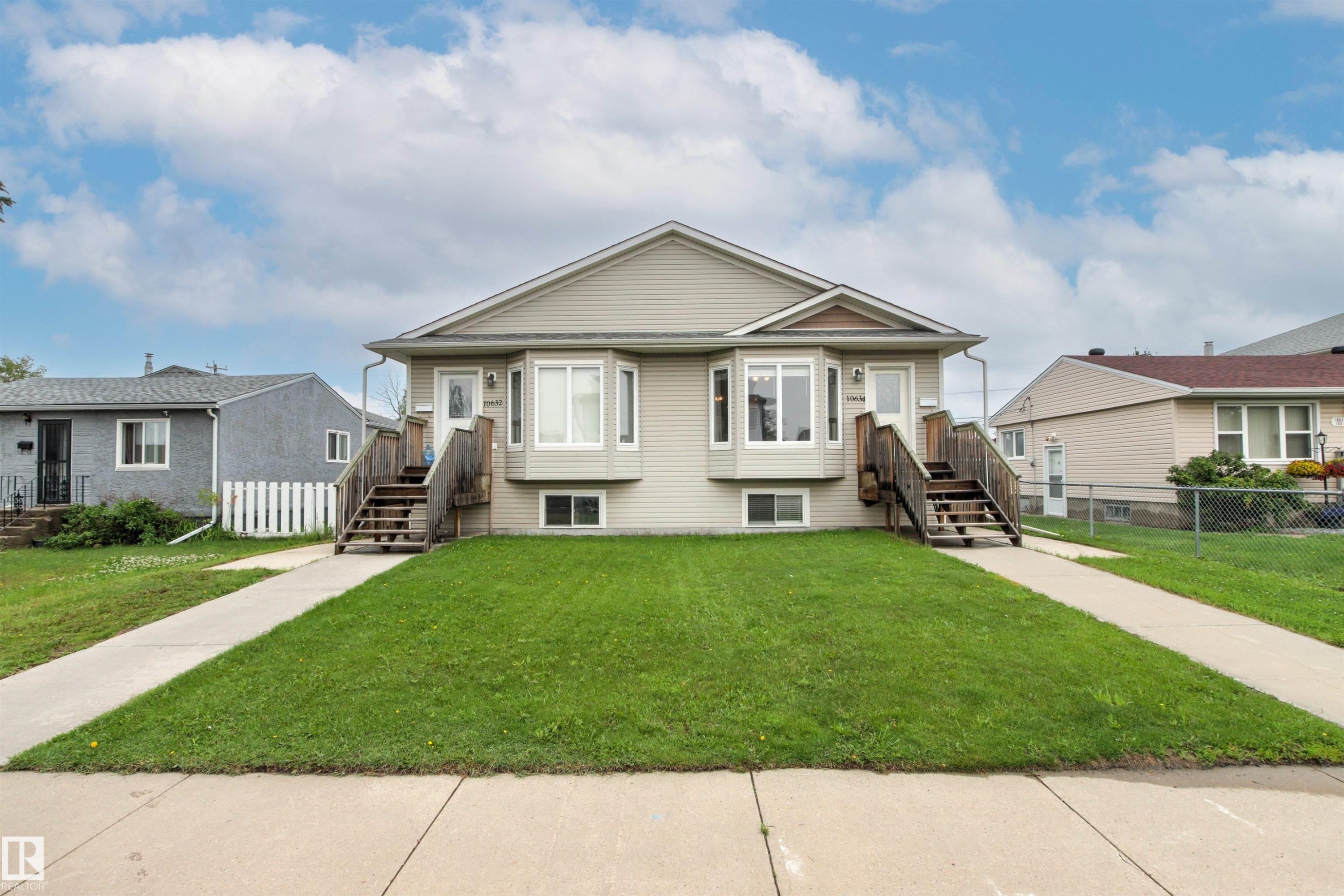Duplex exterior featuring light-toned siding, twin bay windows, and individual wooden staircases leading to separate entrances - 10634 155 Street Nw, Edmonton, AB - Outdoor With Facade