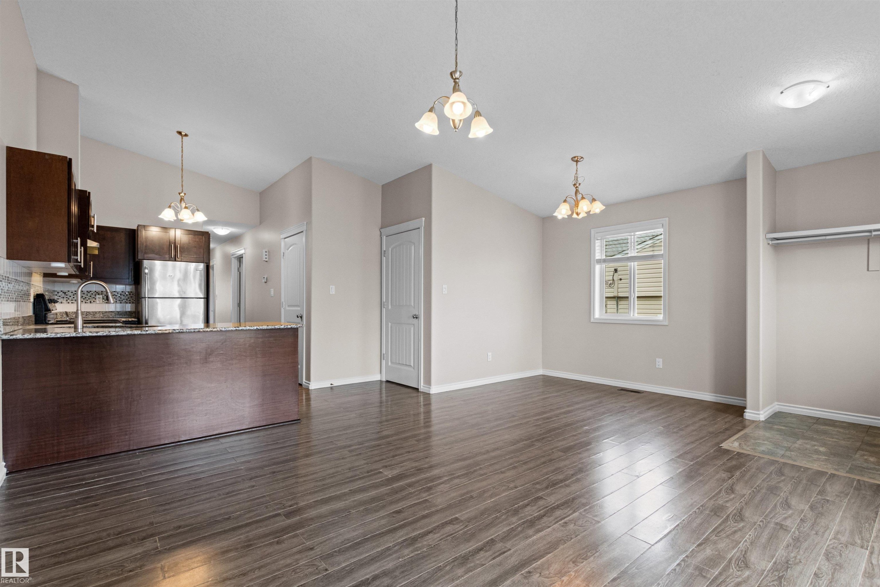Open concept living space featuring wood-finish flooring, a kitchen with dark cabinetry and stainless steel appliances, a breakfast bar with a stone-finish countertop, and a window providing natural light - 10634 155 Street Nw, Edmonton, AB - Indoor Photo Showing Kitchen