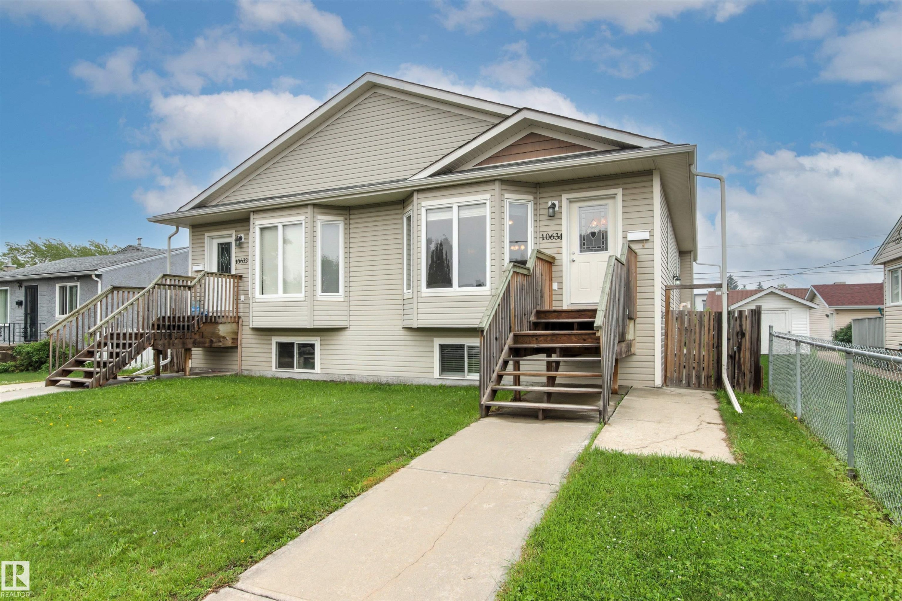 Duplex exterior featuring light-toned siding, two separate front entrances with wooden staircases, and bay windows - 10634 155 Street Nw, Edmonton, AB - Outdoor With Facade