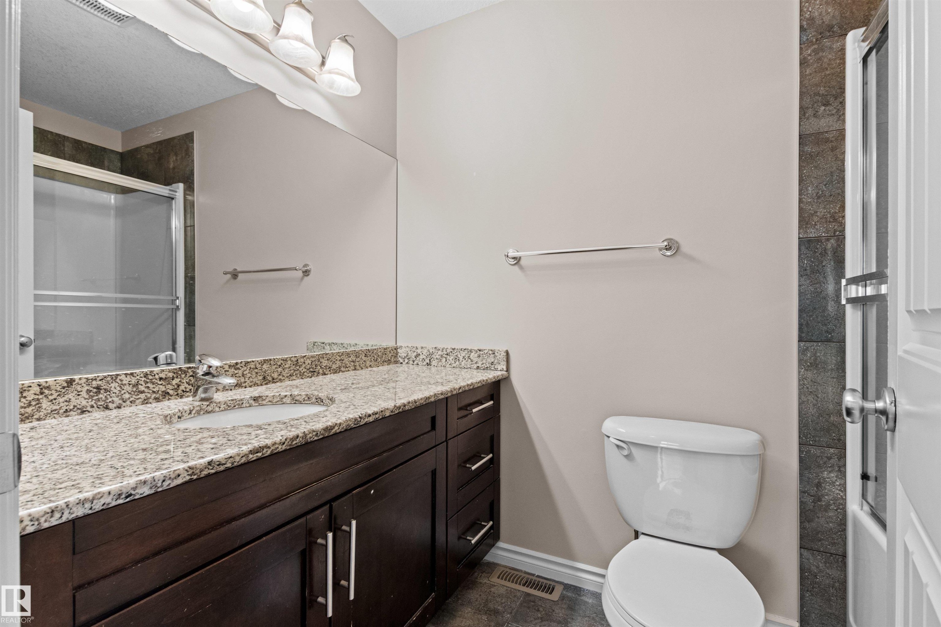 Spacious bathroom featuring a double vanity with stone countertops, dark wood cabinetry, an integrated sink, and a framed shower with a sliding glass door - 10634 155 Street Nw, Edmonton, AB - Indoor Photo Showing Bathroom