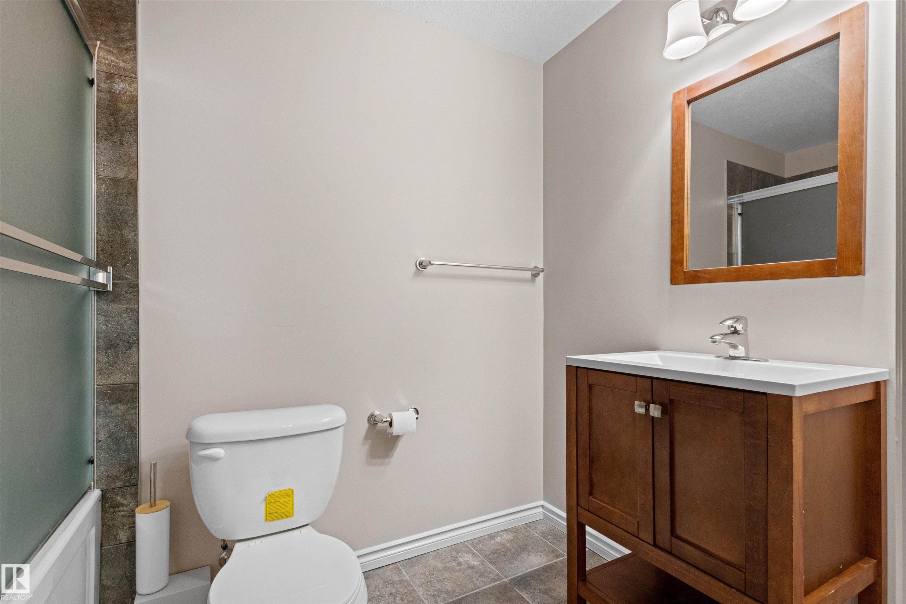 Bathroom featuring a wood-finish vanity with an integrated sink, a framed mirror, and a two-light fixture - 10634 155 Street Nw, Edmonton, AB - Indoor Photo Showing Bathroom