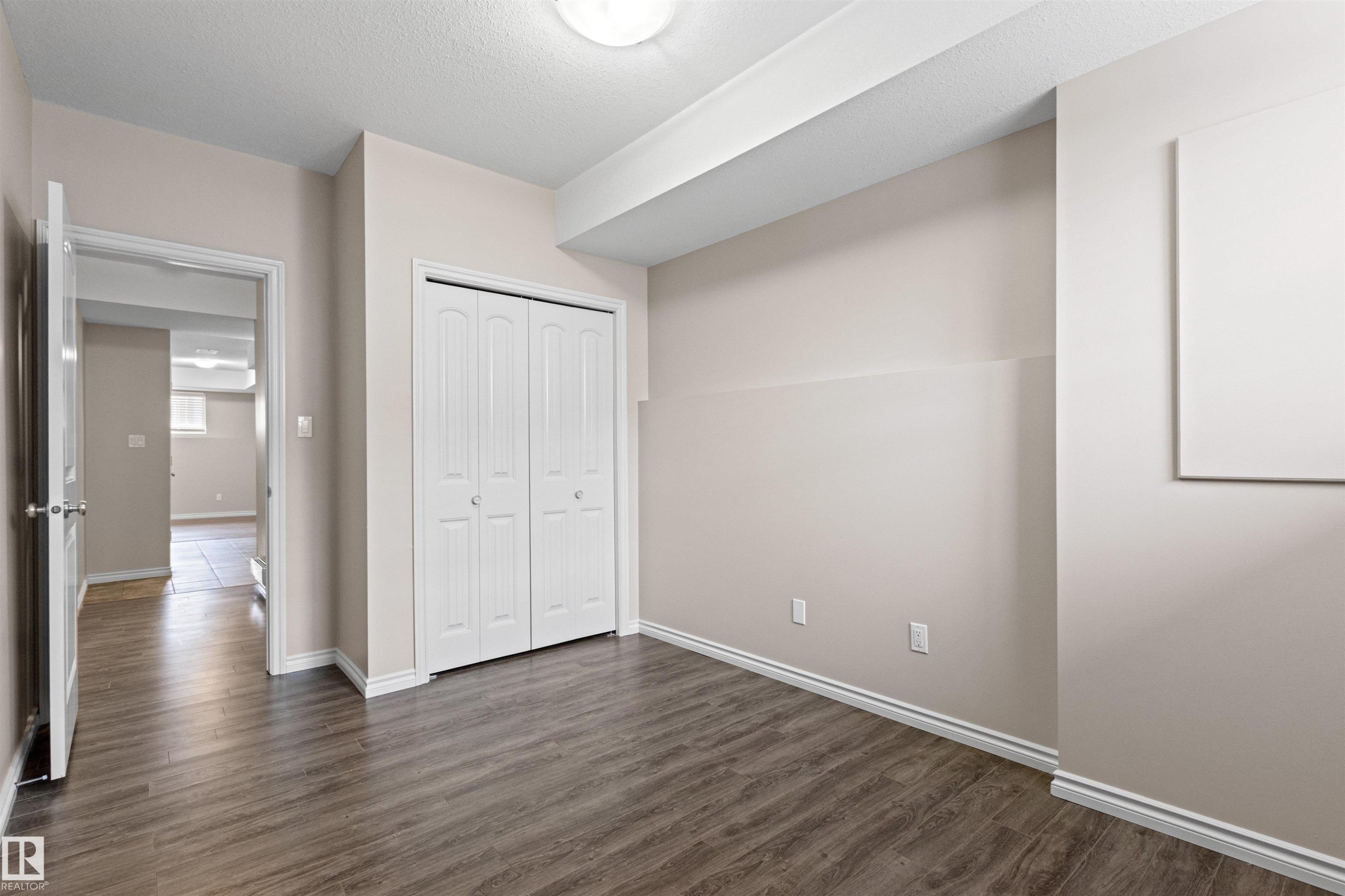 Room featuring wood-finish flooring, neutral wall paint, and a white bi-fold closet door - 10634 155 Street Nw, Edmonton, AB - Indoor Photo Showing Other Room