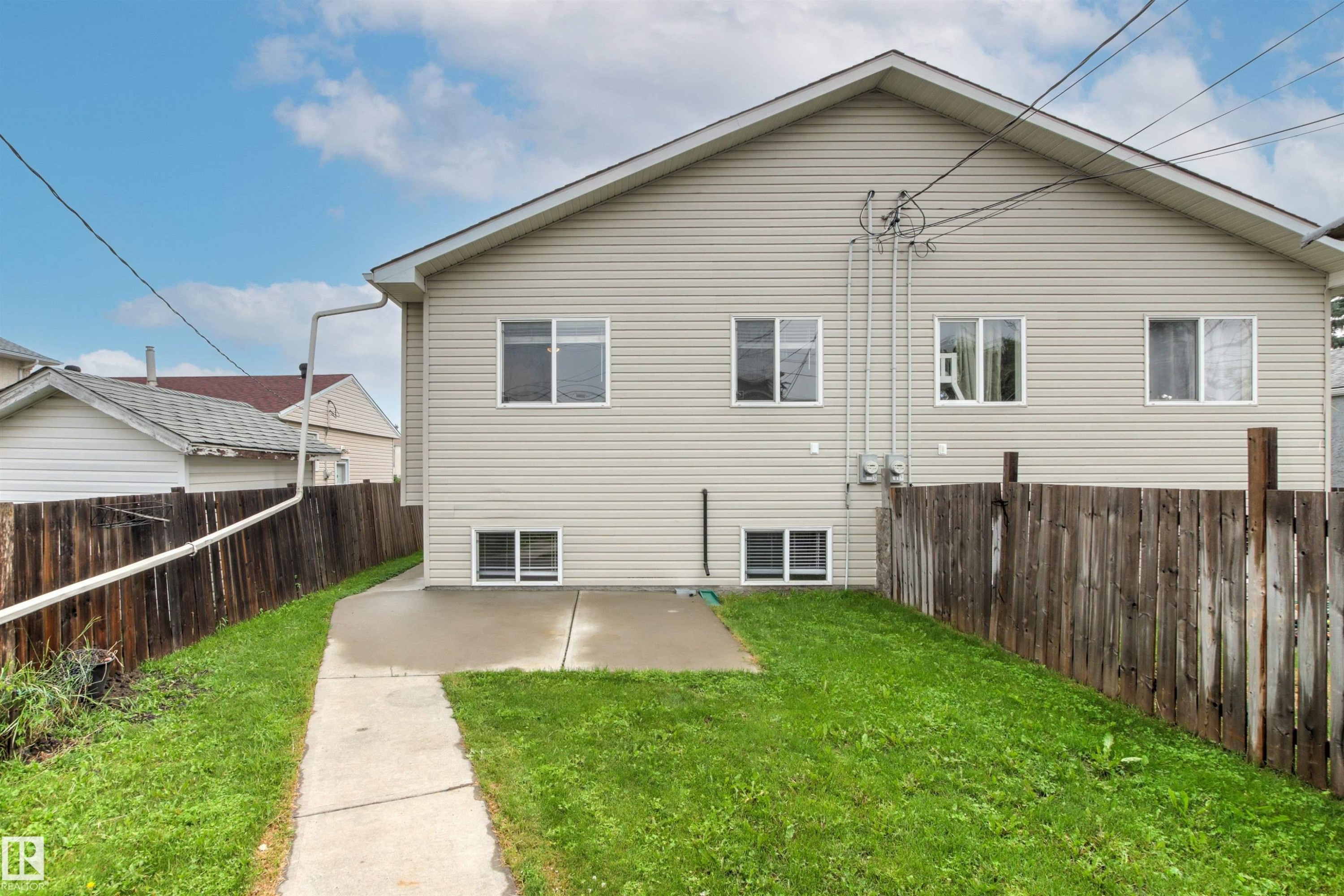 Rear exterior featuring light-colored horizontal siding, multiple windows, and a concrete patio pad - 10634 155 Street Nw, Edmonton, AB - Outdoor With Exterior