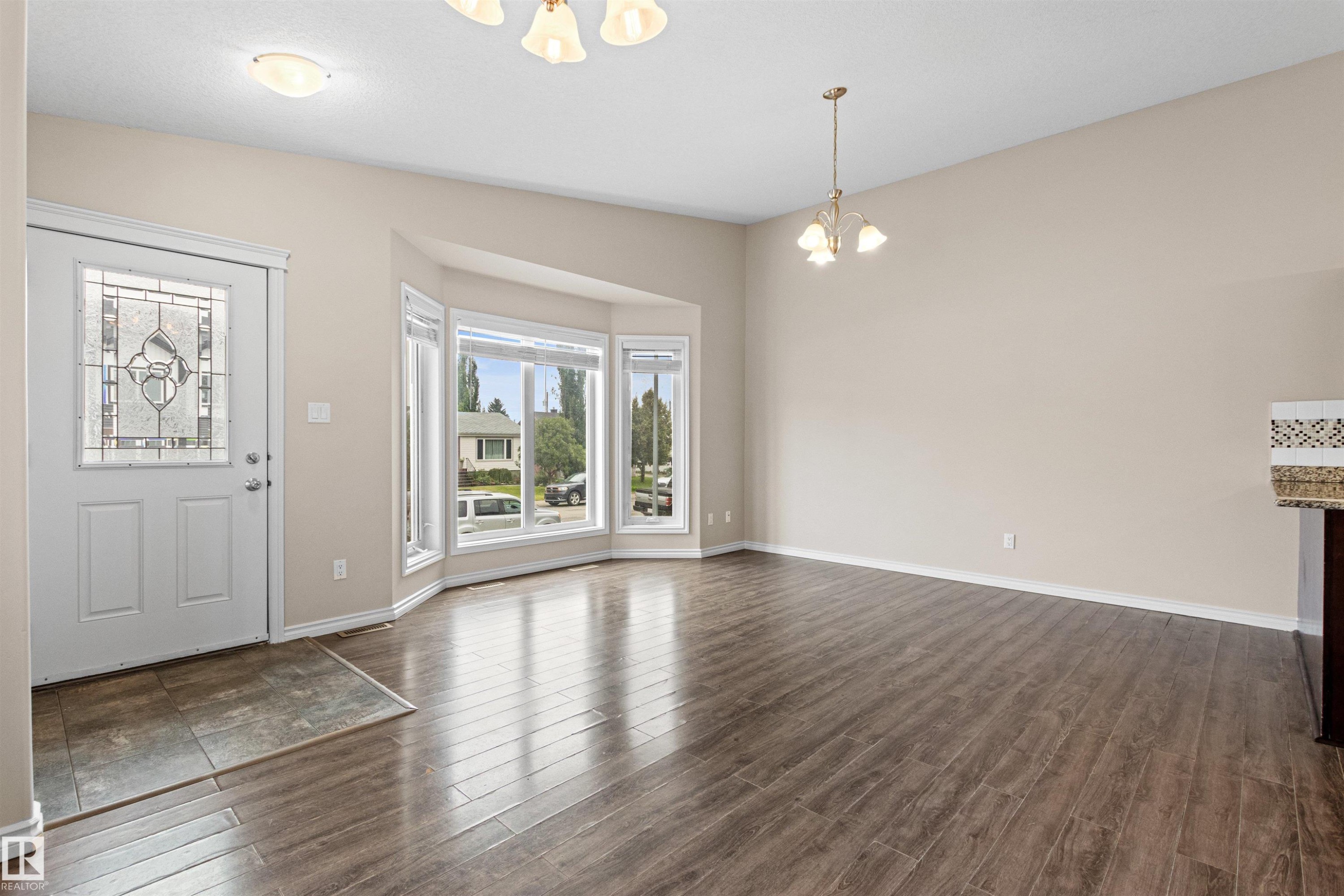 Open-concept main living area featuring wood-finish flooring, a decorative glass entry door, and a bay window - 10634 155 Street Nw, Edmonton, AB - Indoor Photo Showing Other Room