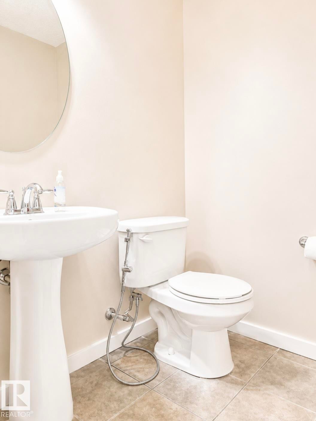 Pedestal sink with chrome faucet, oval wall mirror, white toilet, and tile flooring - 5135 1A Avenue Sw, Edmonton, AB