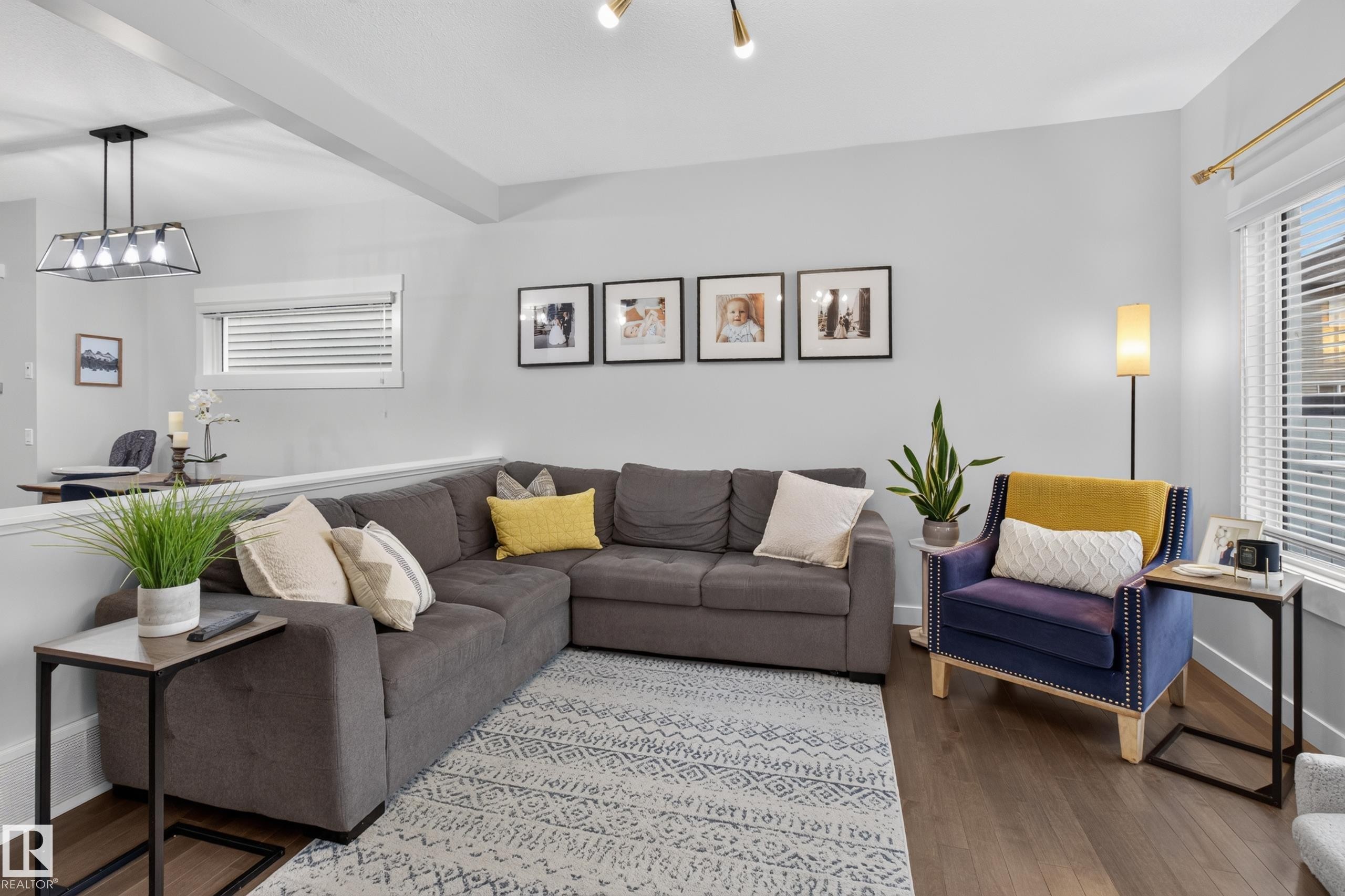 Spacious living area featuring wood-finish flooring, a contemporary light fixture, and large windows with blinds - 17305 73 Street Nw, Edmonton, AB - Indoor Photo Showing Living Room