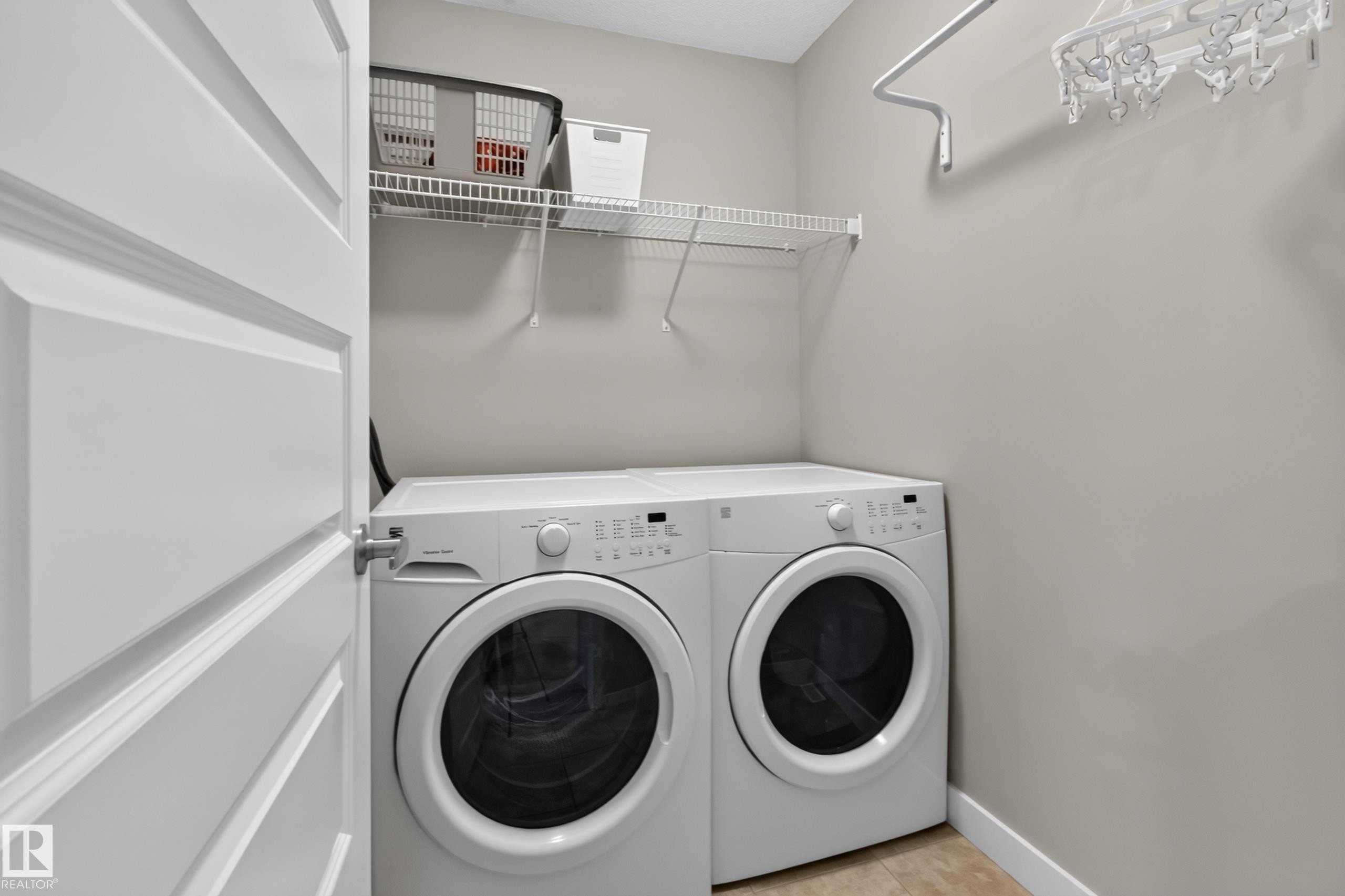 Dedicated laundry area featuring front-loading appliances, overhead wire shelving, and a wall-mounted drying rod - 17305 73 Street Nw, Edmonton, AB - Indoor Photo Showing Laundry Room