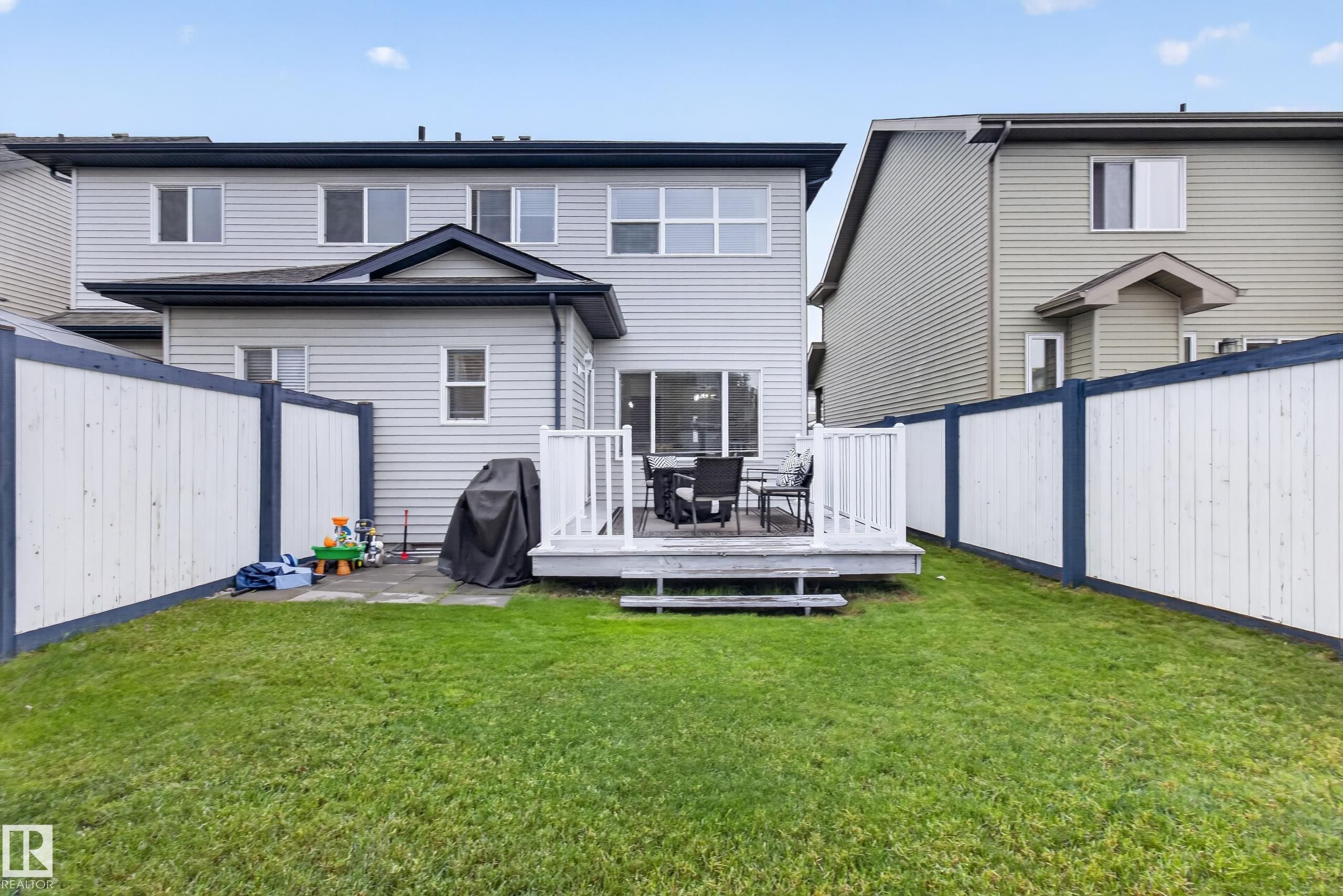 Rear exterior featuring light gray siding, a private backyard with a manicured lawn, a raised wood-finish deck, and a sliding glass door - 17305 73 Street Nw, Edmonton, AB - Outdoor With Deck Patio Veranda With Exterior