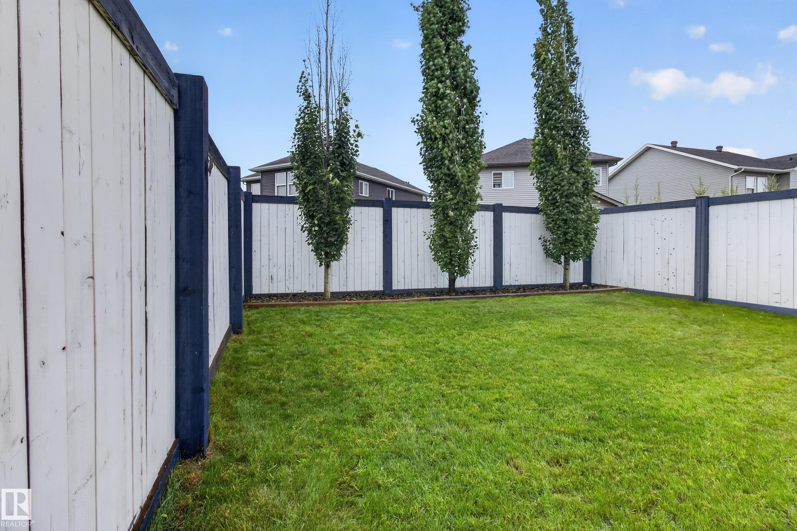 Spacious backyard featuring a lush lawn and perimeter fencing with white panels and dark posts - 17305 73 Street Nw, Edmonton, AB - Outdoor