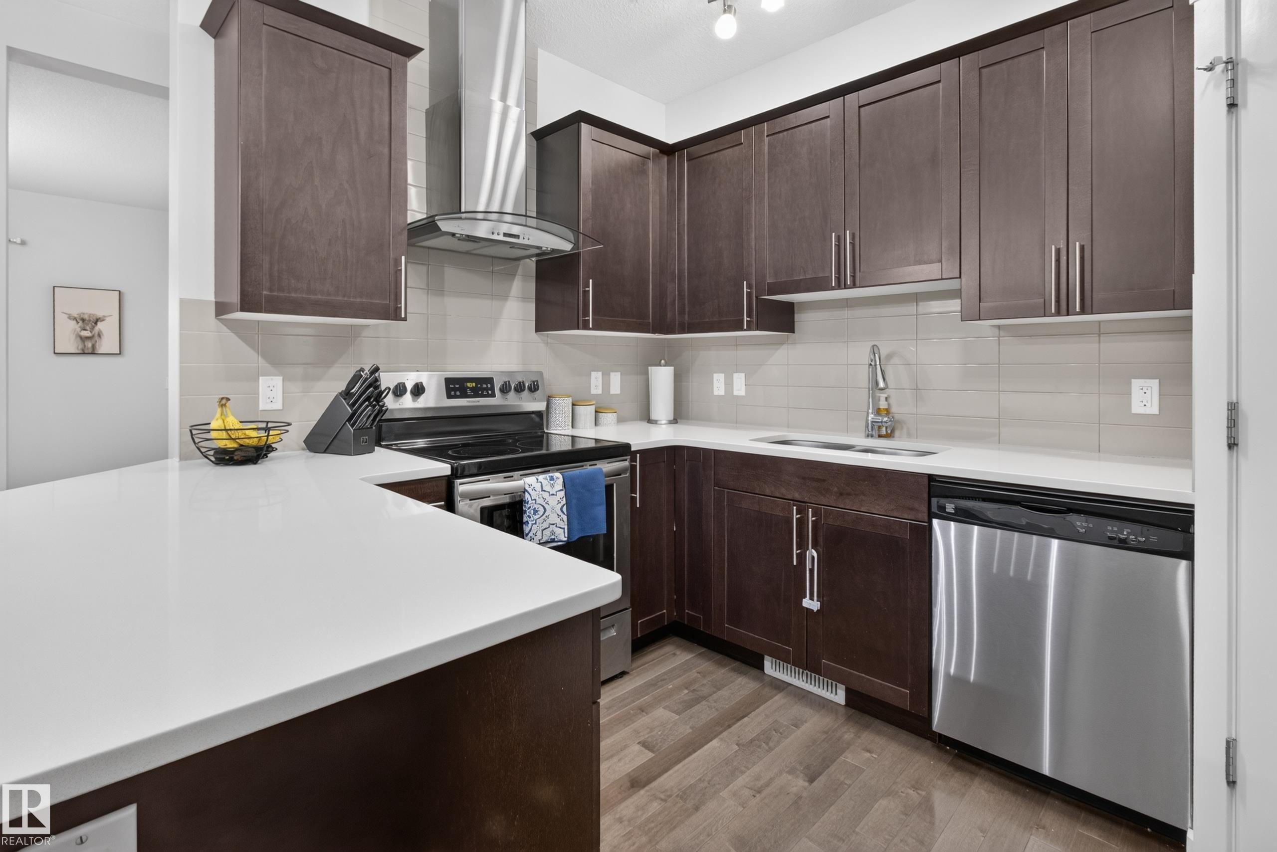 Modern kitchen featuring dark wood cabinetry, light countertops, stainless steel appliances, and a tile backsplash - 17305 73 Street Nw, Edmonton, AB - Indoor Photo Showing Kitchen With Stainless Steel Kitchen With Upgraded Kitchen