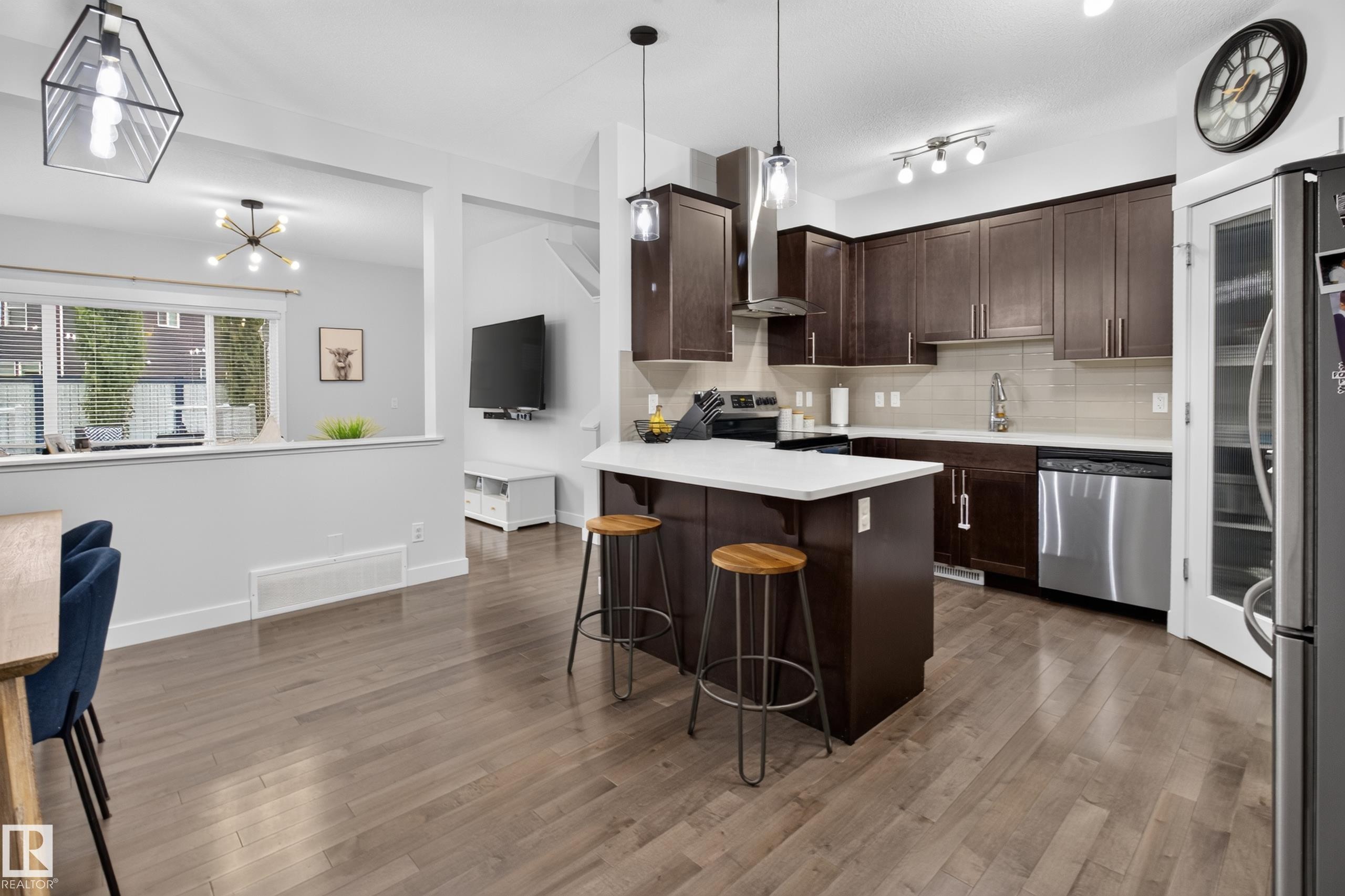 Kitchen featuring dark wood-finish cabinetry, stainless steel appliances, a white island countertop, and light wood-finish flooring - 17305 73 Street Nw, Edmonton, AB - Indoor Photo Showing Kitchen With Stainless Steel Kitchen With Upgraded Kitchen