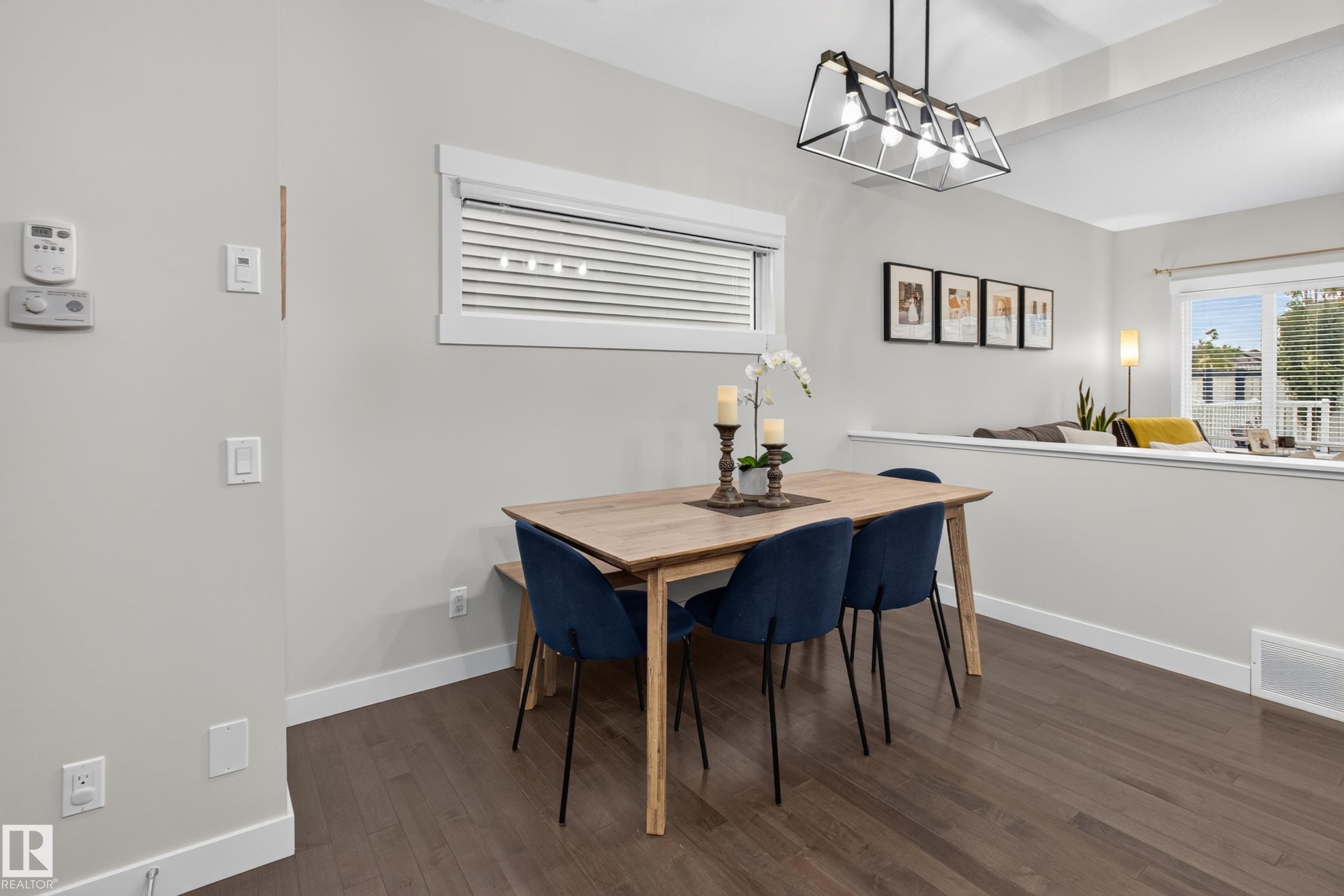 Open-concept dining area featuring wood-finish flooring and a contemporary linear chandelier - 17305 73 Street Nw, Edmonton, AB - Indoor Photo Showing Dining Room