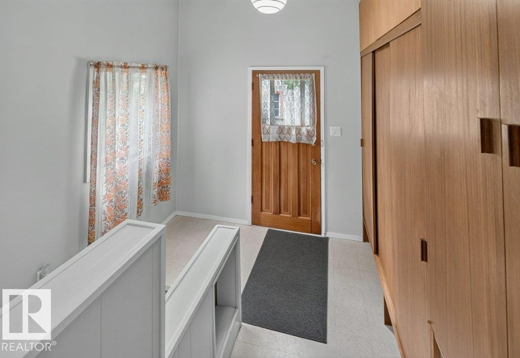 Wood-paneled door, integrated wood-finish cabinetry with recessed pulls, light-colored flooring, and ceiling-mounted light fixture - 9026 92 Street Nw, Edmonton, AB - Indoor Photo Showing Other Room