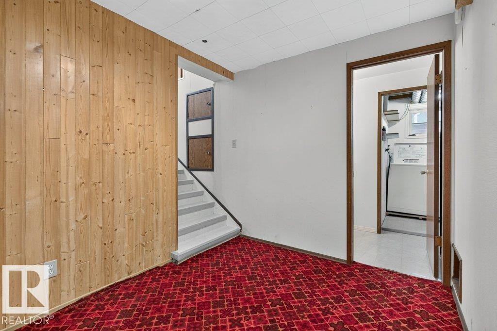 Wood-paneled wall, white painted walls, patterned red carpet, interior staircase with white treads, and a doorway leading to a utility space - 9026 92 Street Nw, Edmonton, AB - Indoor Photo Showing Other Room