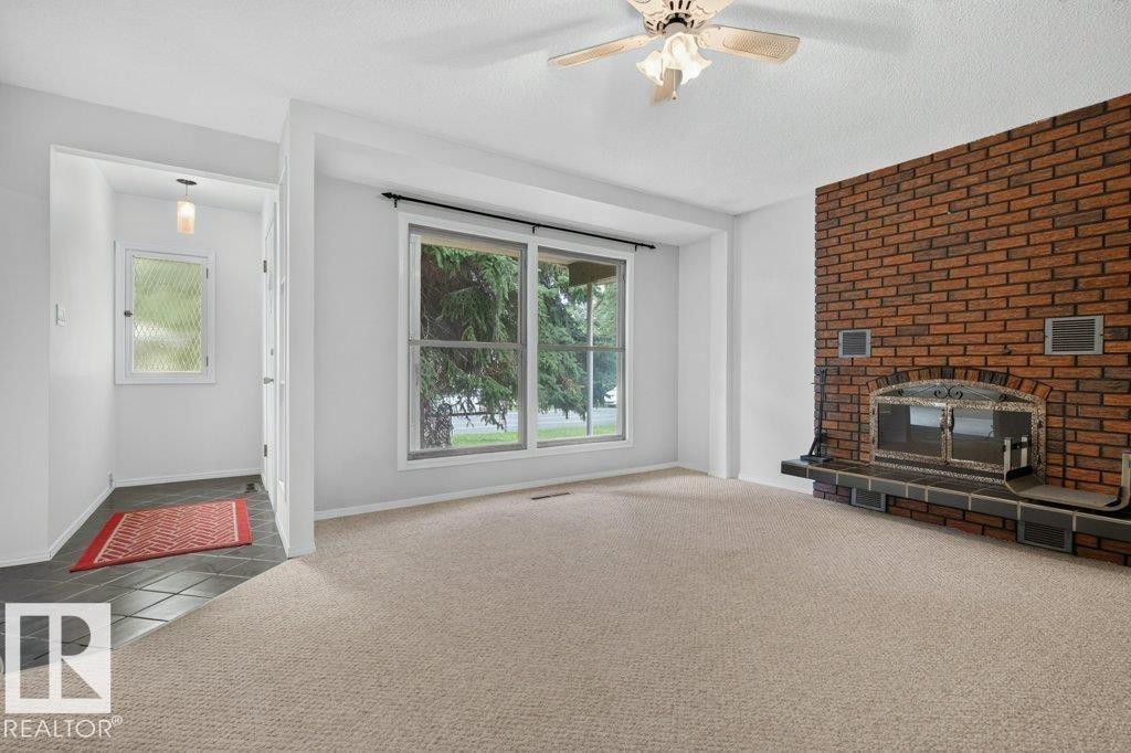 Brick-faced fireplace with hearth, ceiling fan, carpeted flooring, large window, and tiled entry - 9026 92 Street Nw, Edmonton, AB - Indoor With Fireplace