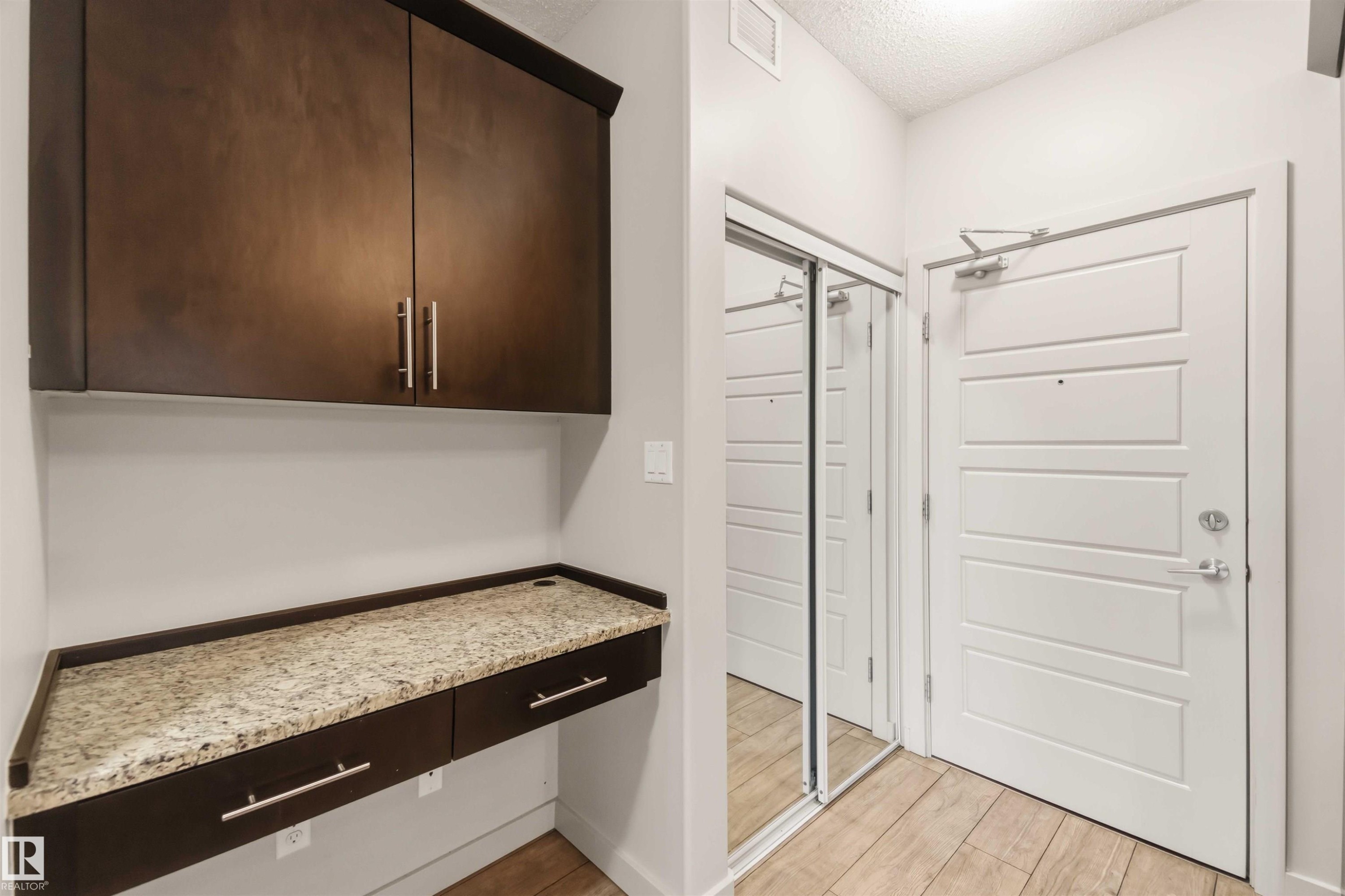 Built-in desk with a stone-finish countertop, dark wood-finish cabinetry, and a mirrored closet - #414 5510 Schonsee Dr Nw, Edmonton, AB