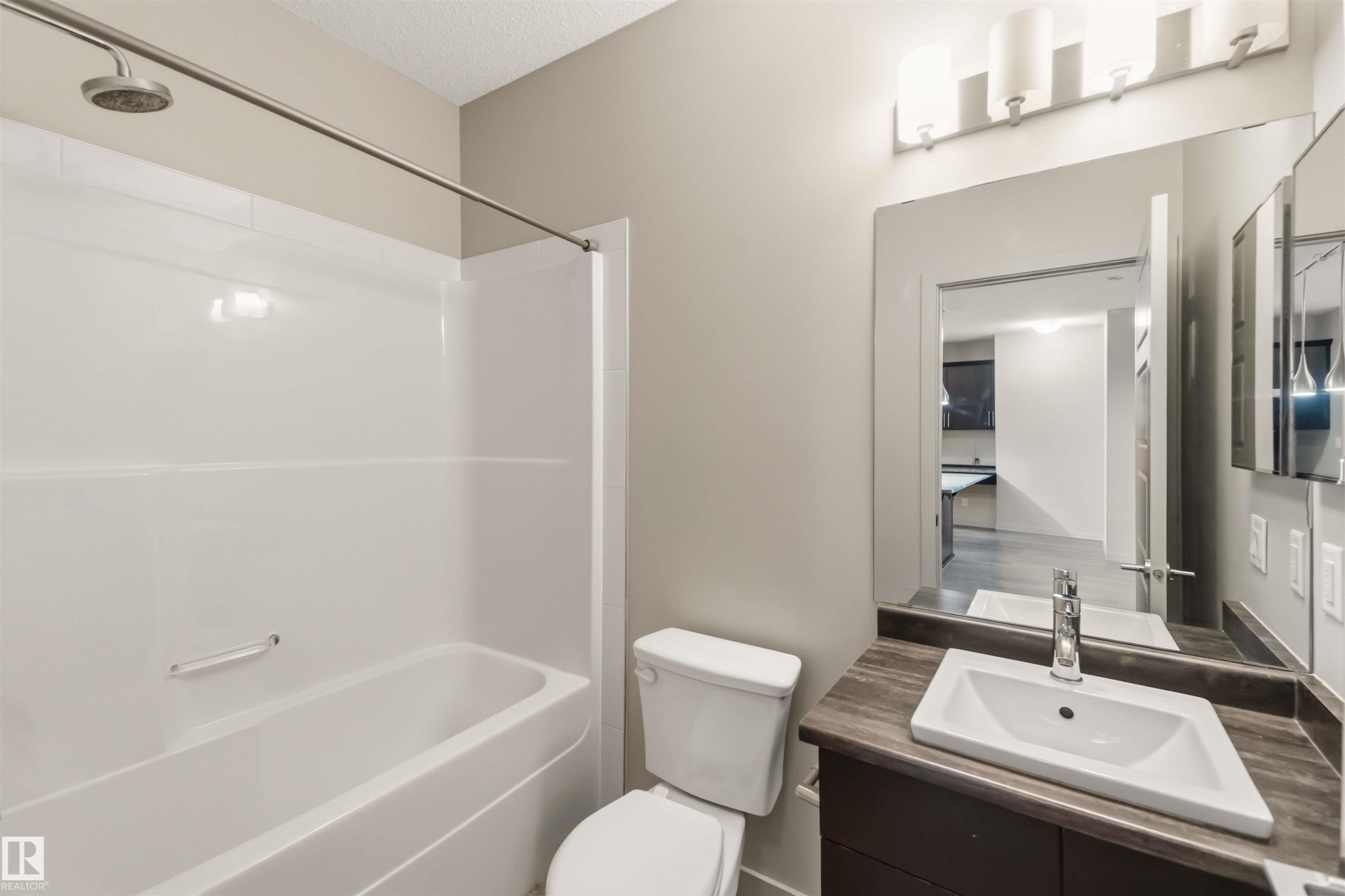 Bathroom featuring a combination shower and tub, a vanity with an integrated sink, a large mirror, and a wall-mounted light fixture - #414 5510 Schonsee Dr Nw, Edmonton, AB