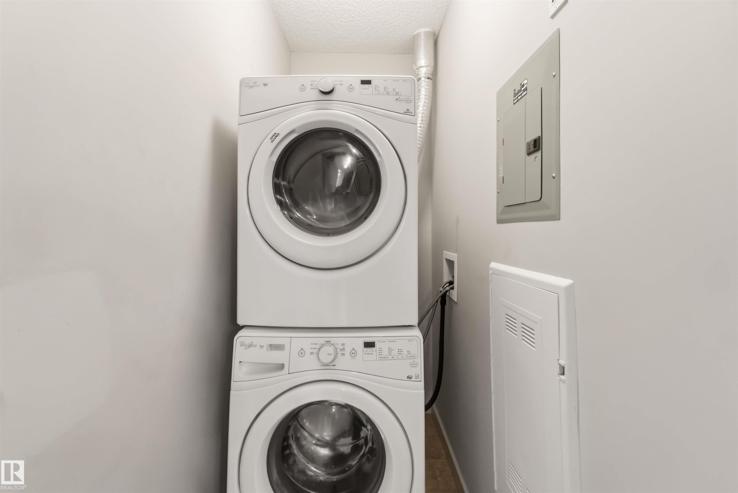 Stacked laundry appliances with front-load design, recessed utility panel, and wood-finish flooring - #414 5510 Schonsee Dr Nw, Edmonton, AB