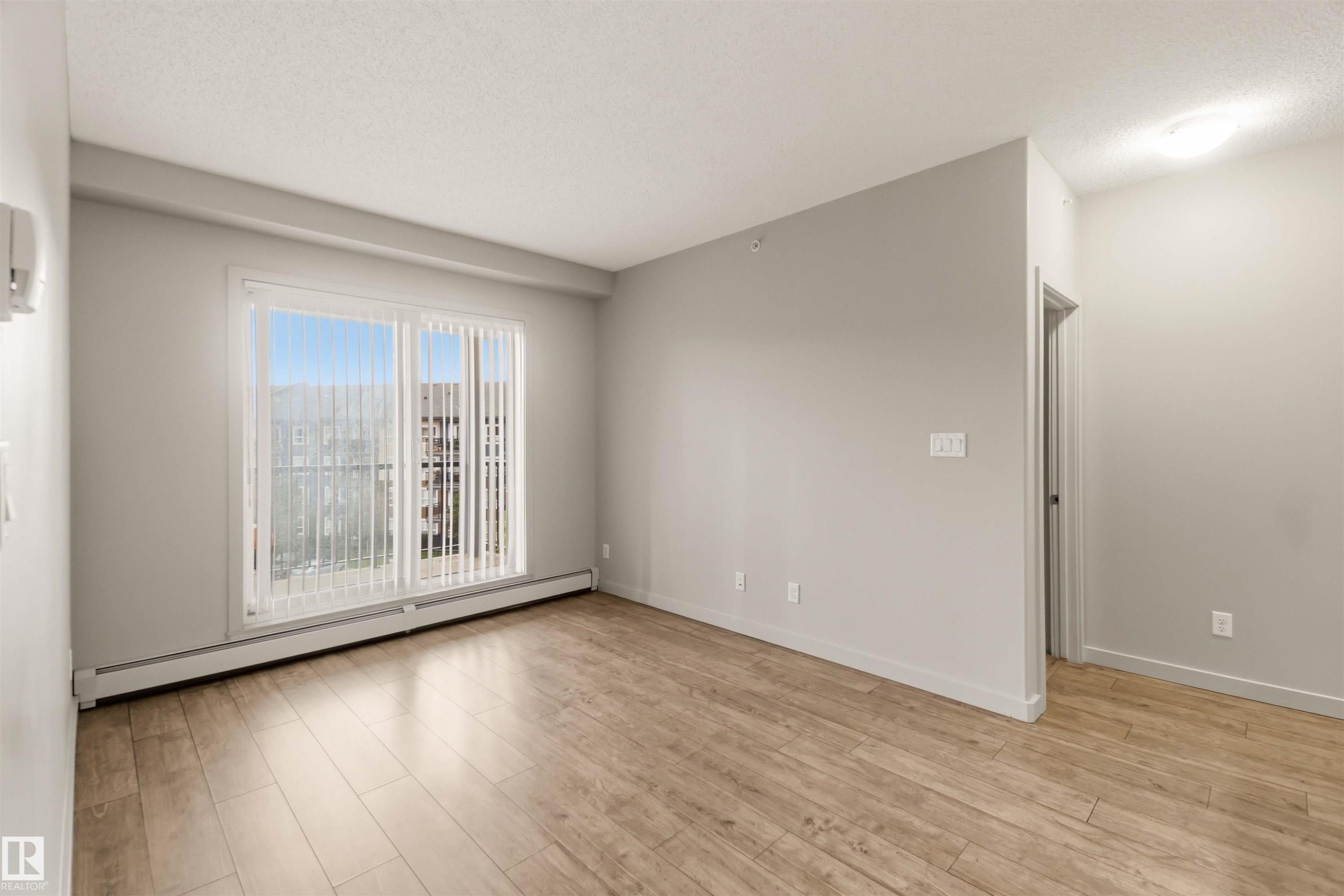 Wood-finish flooring, light grey wall paint, large sliding glass door, white vertical blinds, and a flush mount ceiling light - #414 5510 Schonsee Dr Nw, Edmonton, AB