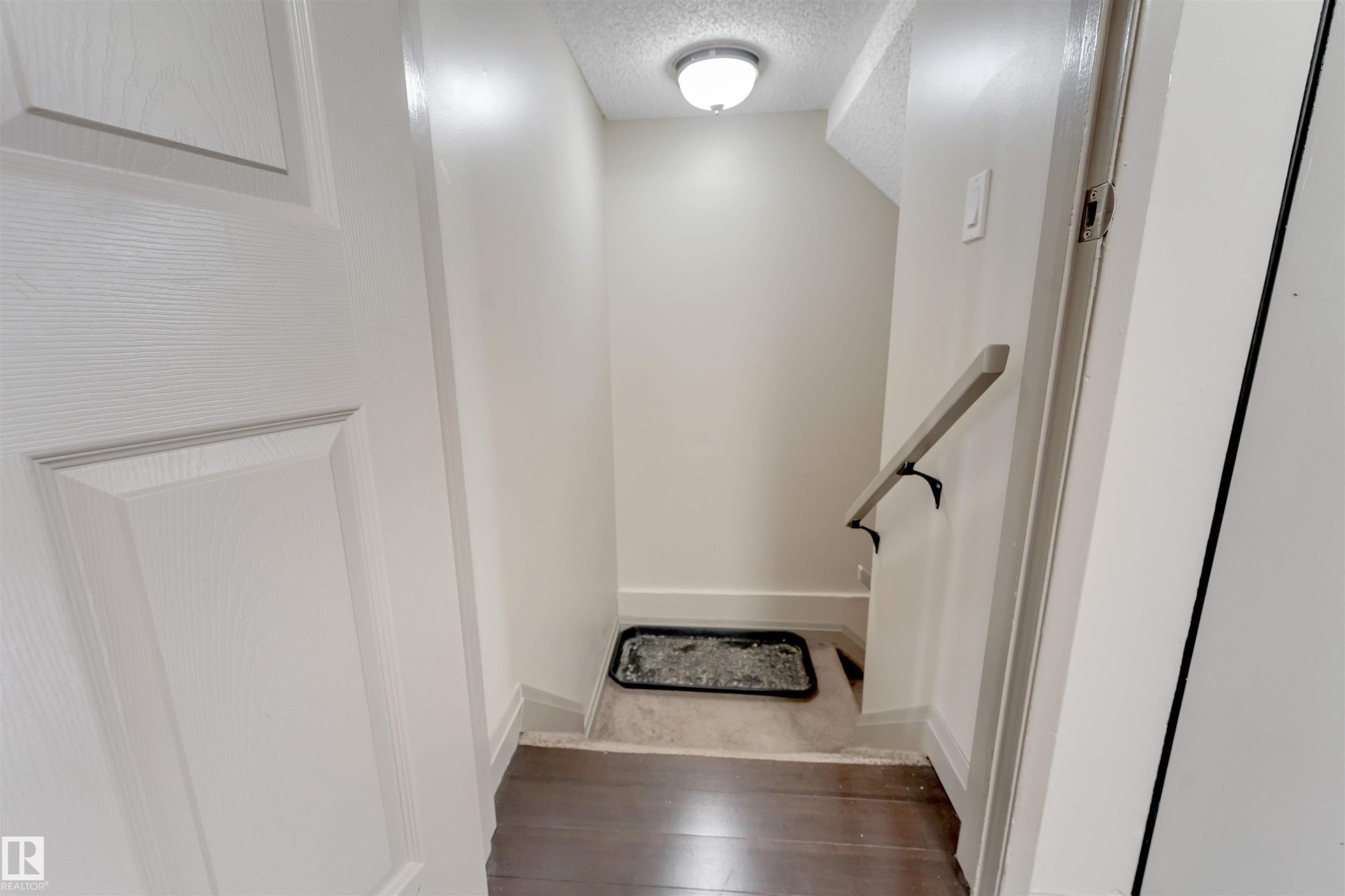 Recessed ceiling light fixture, white interior door with paneling, wood-finish flooring, wall-mounted handrail, and light-toned wall paint - #37 1411 Mill Woods Rd E Nw, Edmonton, AB - Indoor Photo Showing Other Room