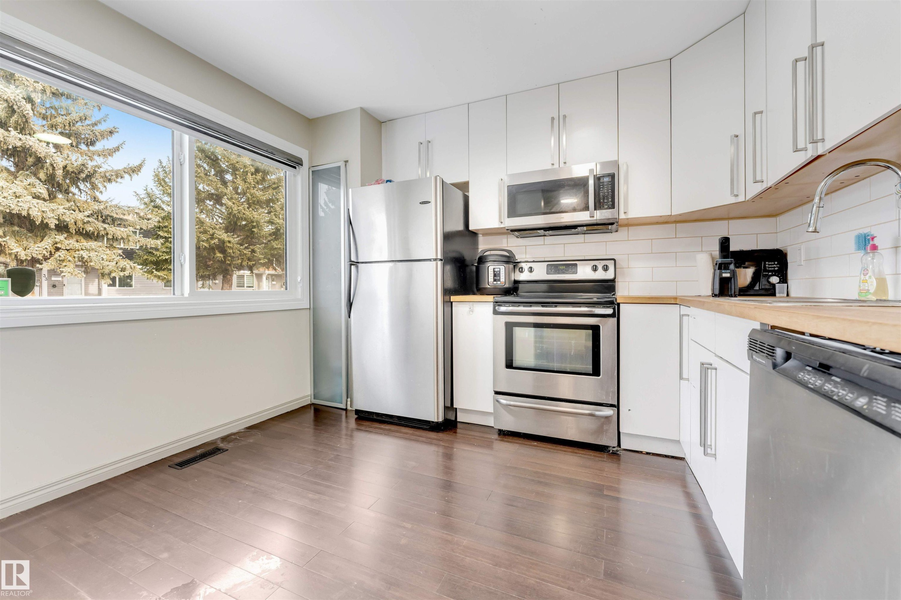 Kitchen featuring stainless steel appliances, white cabinetry, wood-finish countertops, and wood-finish flooring - #37 1411 Mill Woods Rd E Nw, Edmonton, AB - Indoor Photo Showing Kitchen