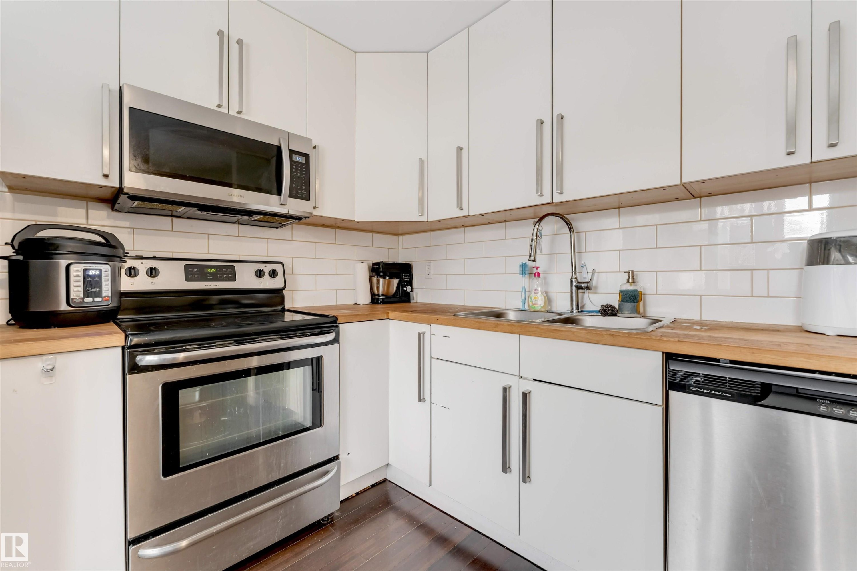 Kitchen featuring stainless steel appliances, white cabinetry, wood-finish countertops, subway tile backsplash, and wood-finish flooring - #37 1411 Mill Woods Rd E Nw, Edmonton, AB - Indoor Photo Showing Kitchen With Double Sink