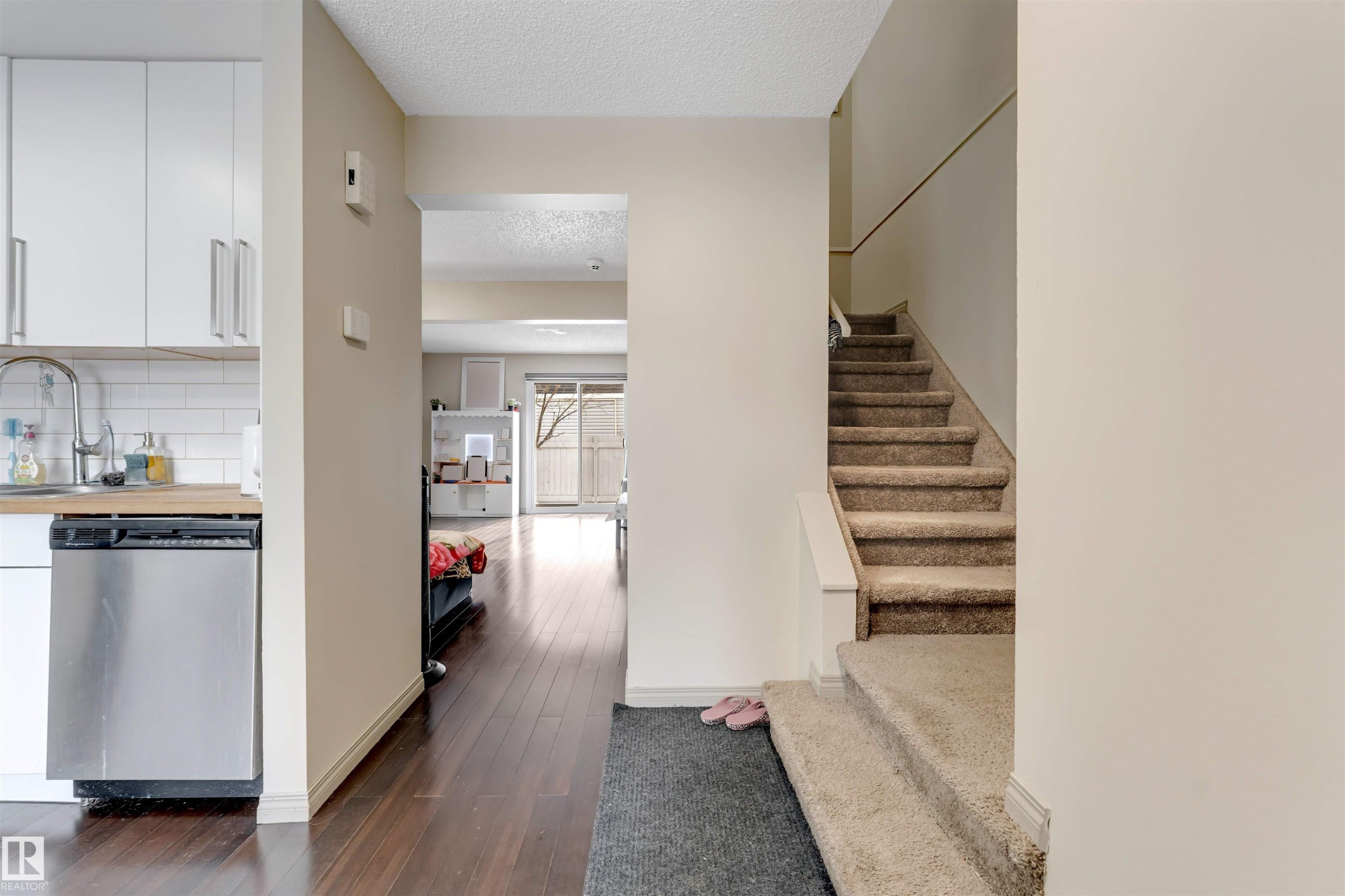 Stainless steel dishwasher, white subway tile backsplash, wood-finish flooring, and carpeted staircase - #37 1411 Mill Woods Rd E Nw, Edmonton, AB - Indoor Photo Showing Other Room