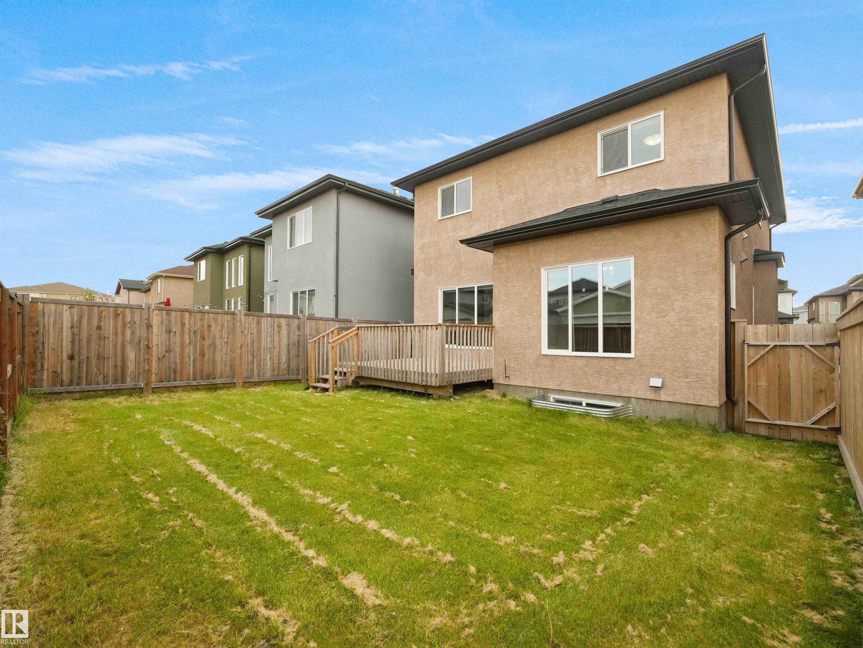 Expansive grassed yard with a wooden privacy fence, featuring a raised wood deck with railing and steps, and a stucco exterior - 17020 62 Street Nw, Edmonton, AB - Outdoor With Exterior